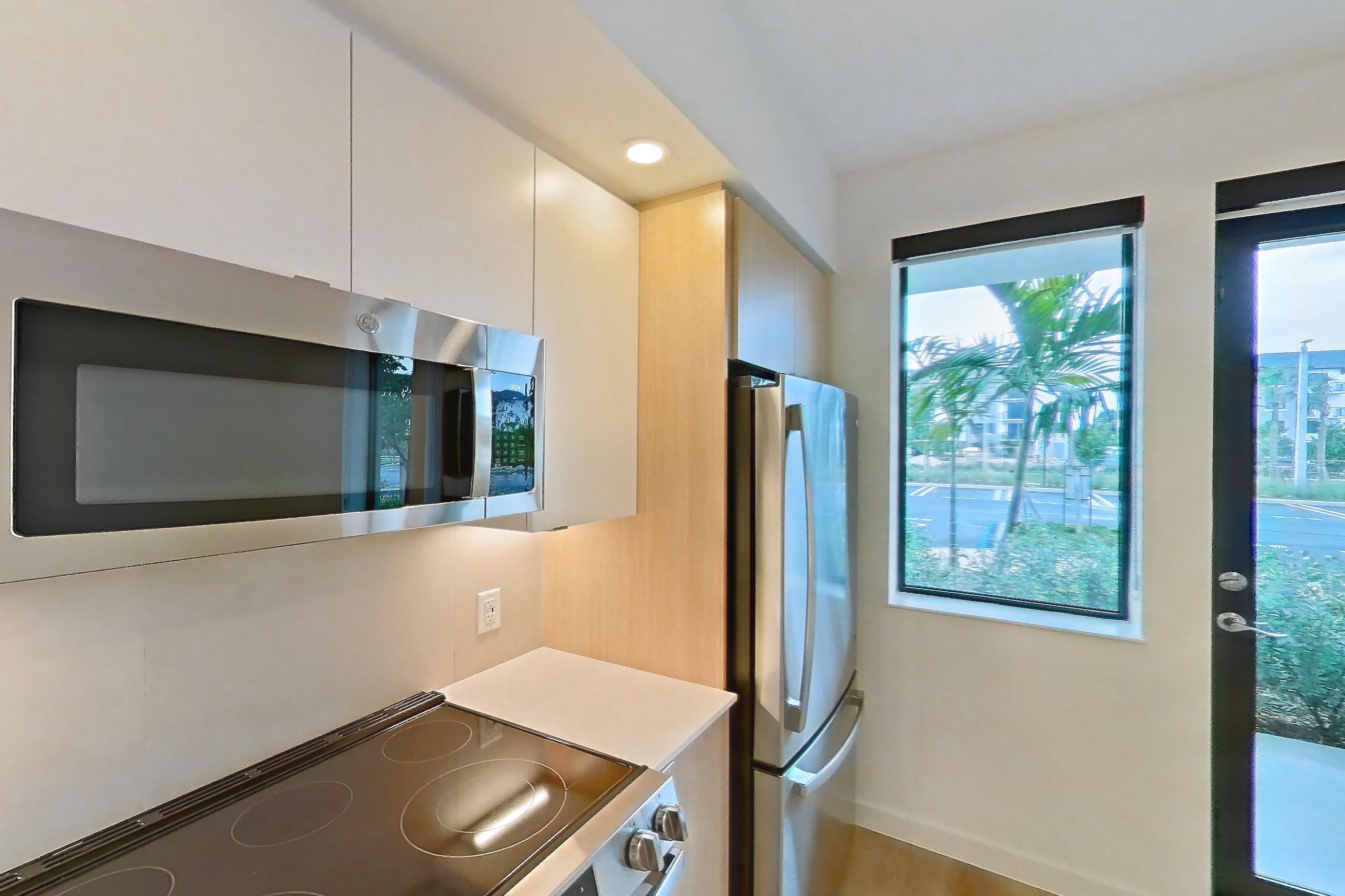 Kitchen with electric range, light countertops, light wood-finish flooring, microwave, oven/range, refrigerator, and stainless steel appliances, Apartment 109 at Caroline Pompano Beach