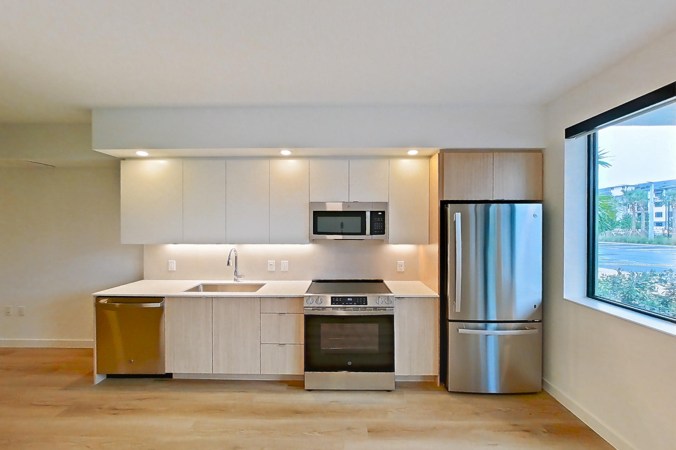 Living room with dishwasher, electric range, light countertops, light wood-finish flooring, oven/range, refrigerator, and stainless steel appliances, Apartment 109 at Caroline Pompano Beach