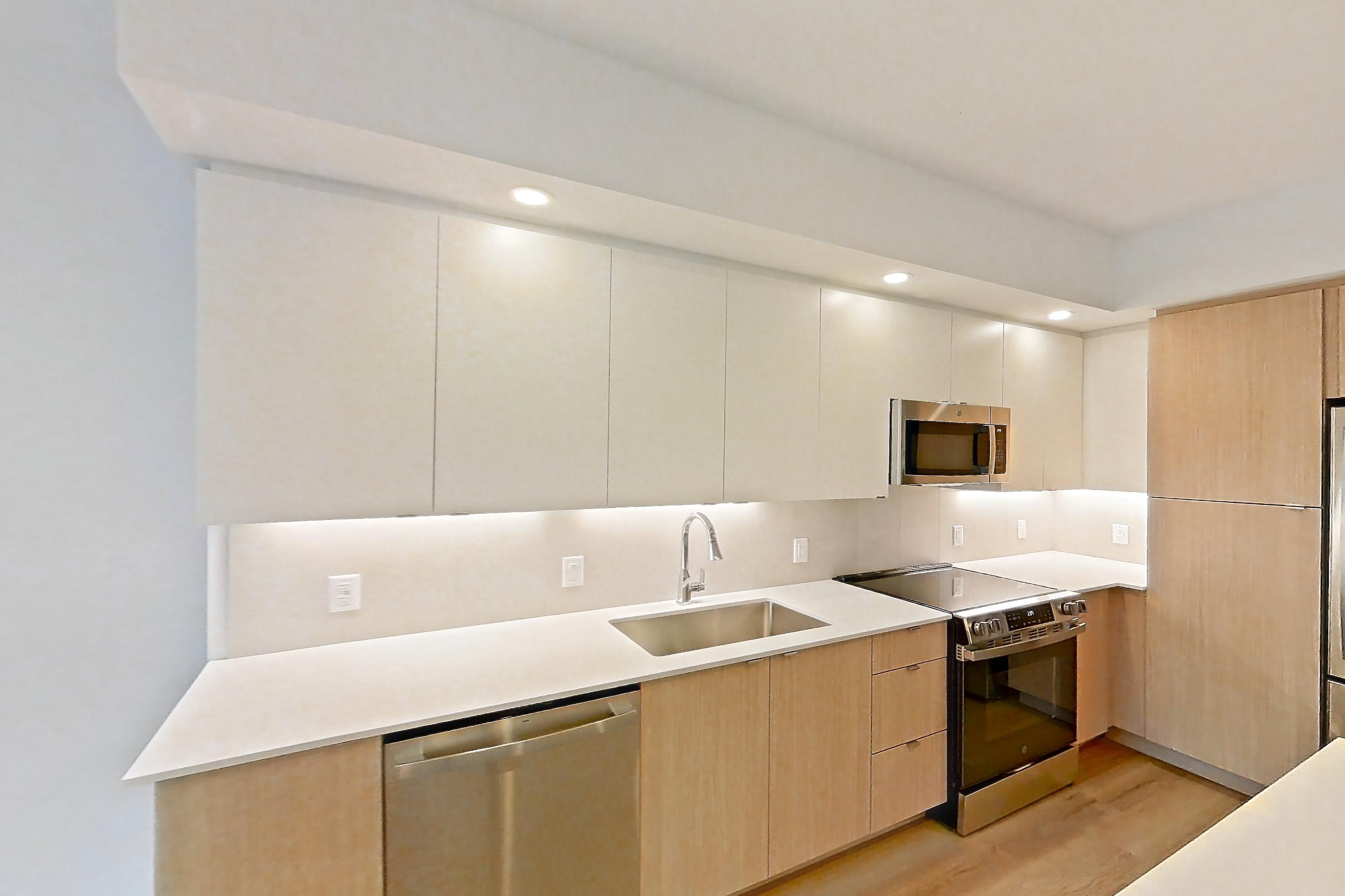 Kitchen island corner with dishwasher, light stone countertops, light wood-finish flooring, and stainless steel appliances, Apartment 110 at Caroline Pompano Beach