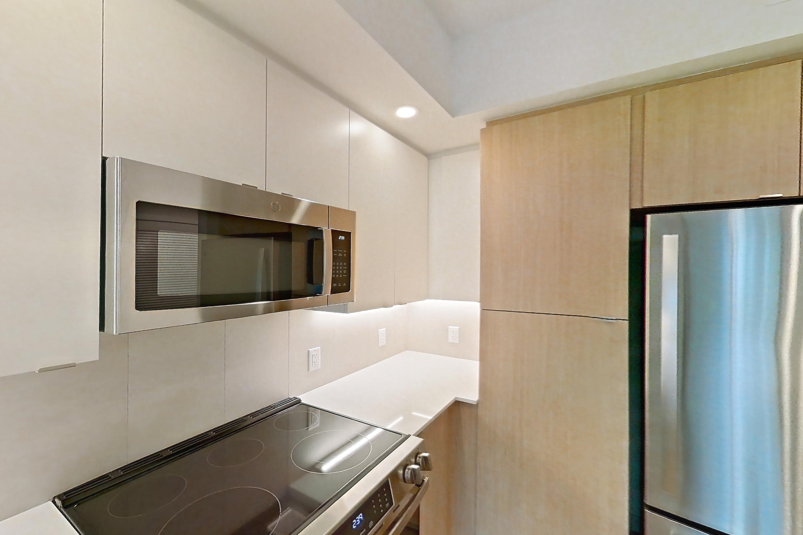 Kitchen with dishwasher, electric range, light countertops, light stone countertops, light wood-finish flooring, microwave, oven/range, refrigerator, and stainless steel appliances, Apartment 110 at Caroline Pompano Beach