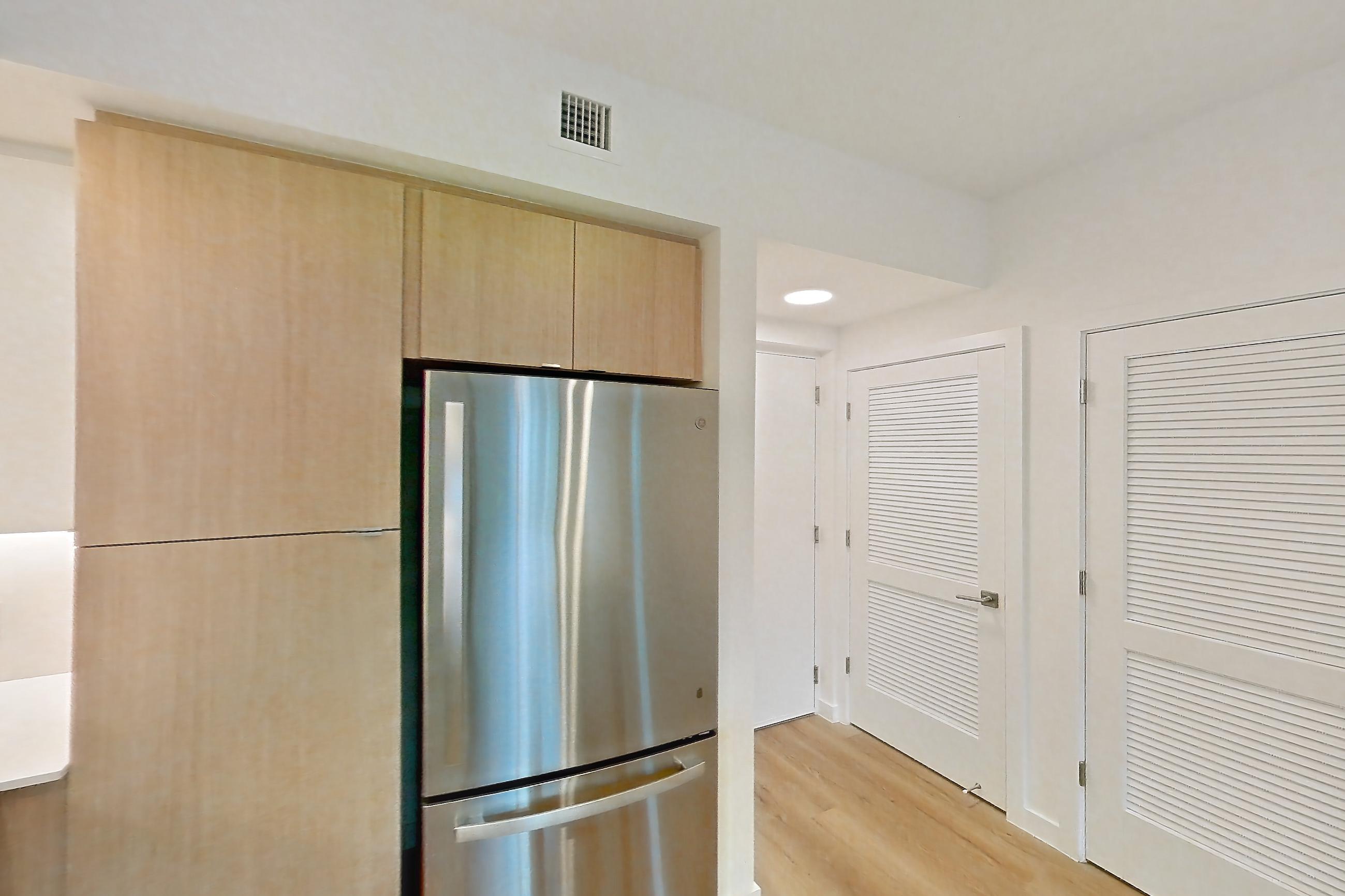 Kitchen with dishwasher, electric range, light countertops, light stone countertops, light wood-finish flooring, microwave, oven/range, refrigerator, and stainless steel appliances, Apartment 110 at Caroline Pompano Beach