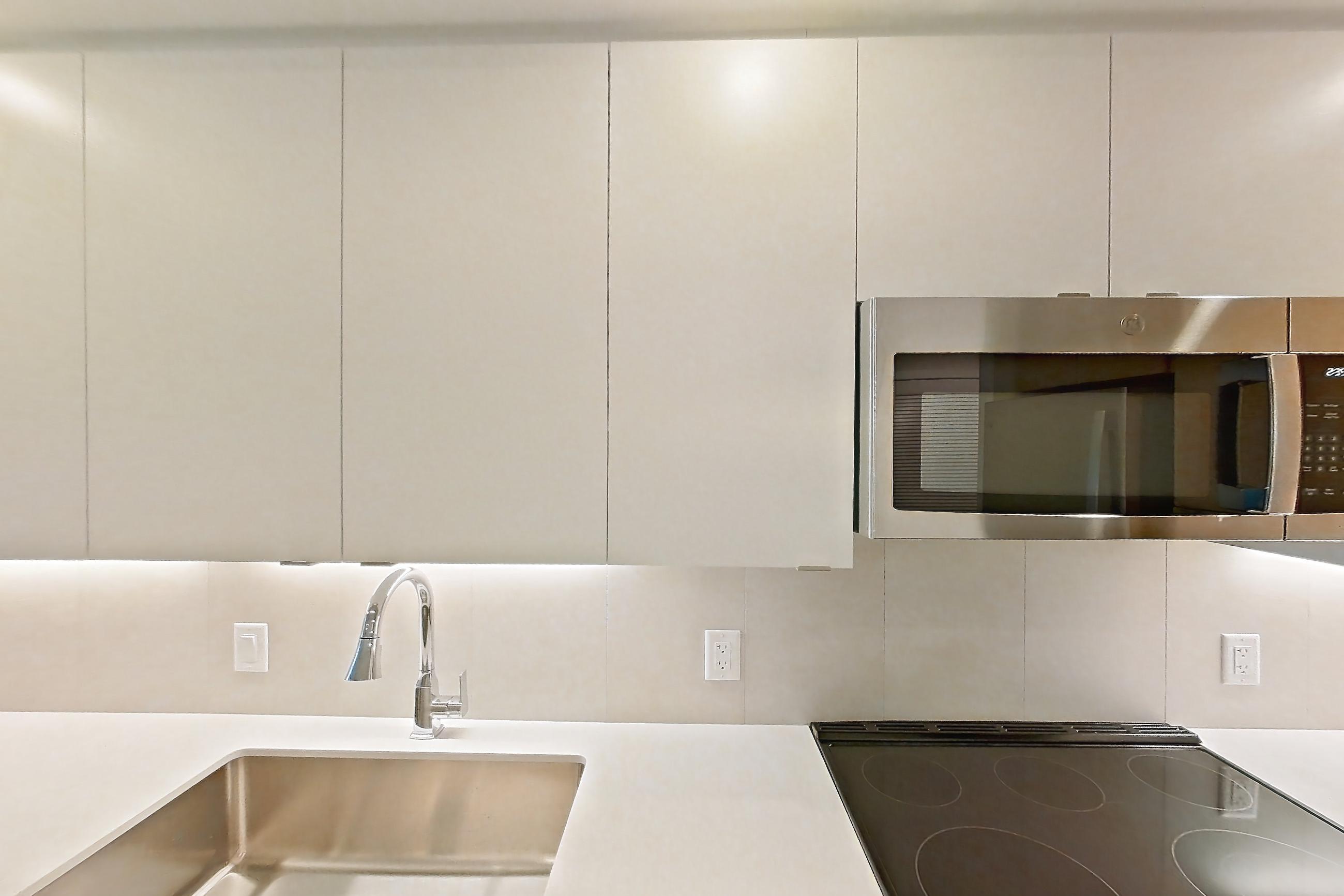 Kitchen with dishwasher, electric range, light countertops, light stone countertops, light wood-finish flooring, microwave, oven/range, refrigerator, and stainless steel appliances, Apartment 110 at Caroline Pompano Beach