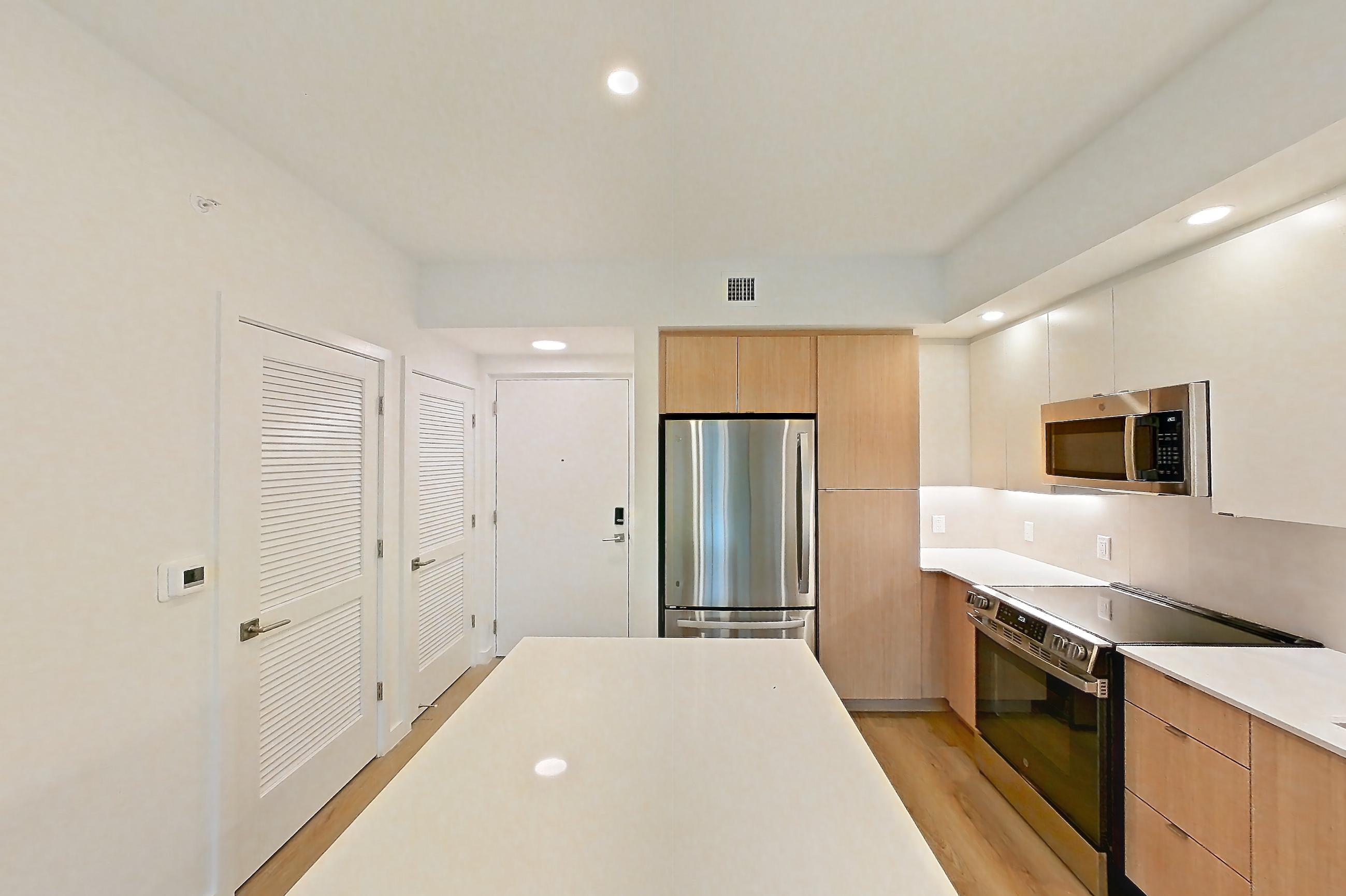 Kitchen island corner with black appliances, dishwasher, light stone countertops, light wood-finish flooring, oven/range, and stainless steel appliances, Apartment 111 at Caroline Pompano Beach