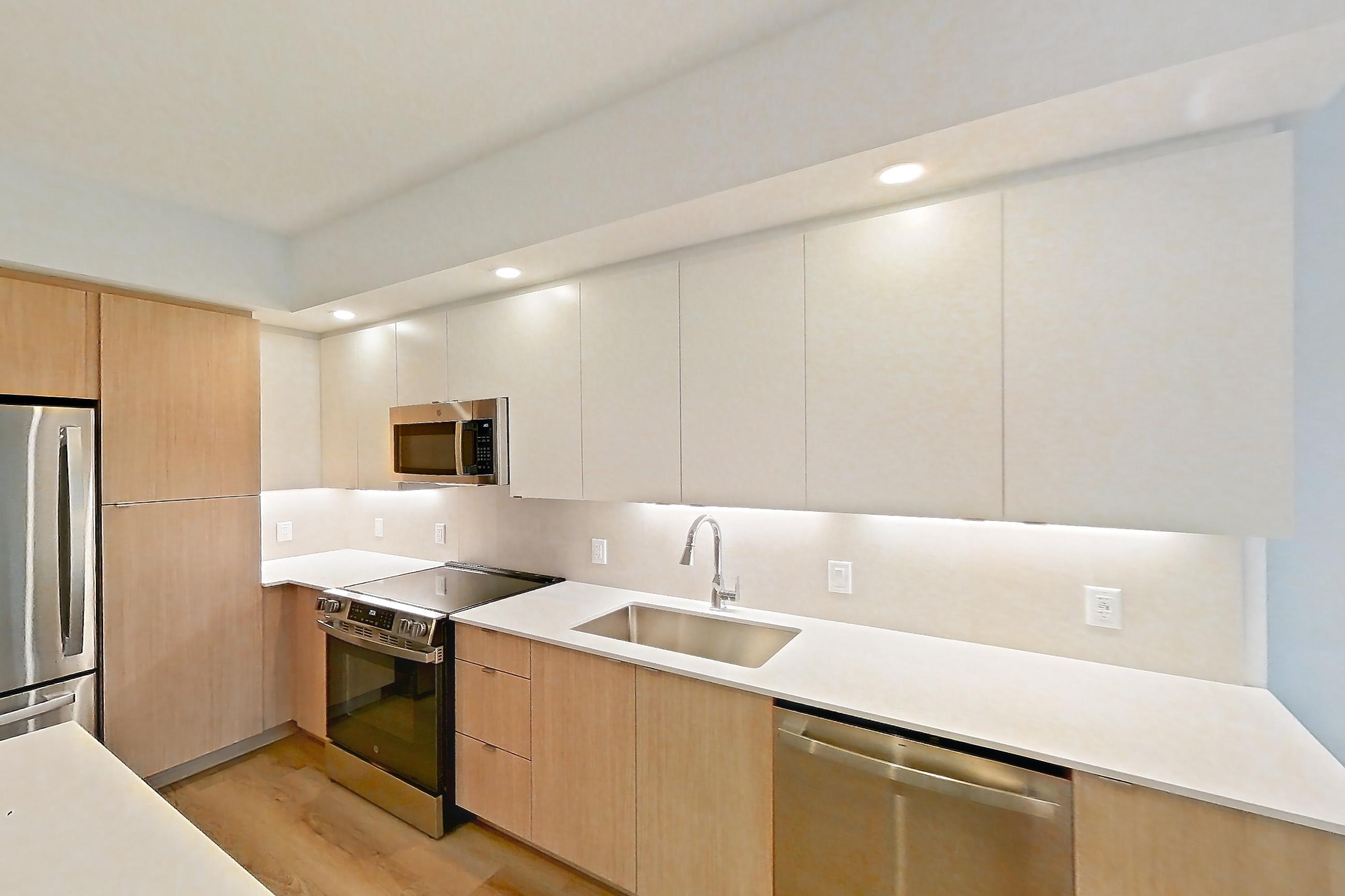 Kitchen island corner with black appliances, dishwasher, light stone countertops, light wood-finish flooring, oven/range, and stainless steel appliances, Apartment 111 at Caroline Pompano Beach