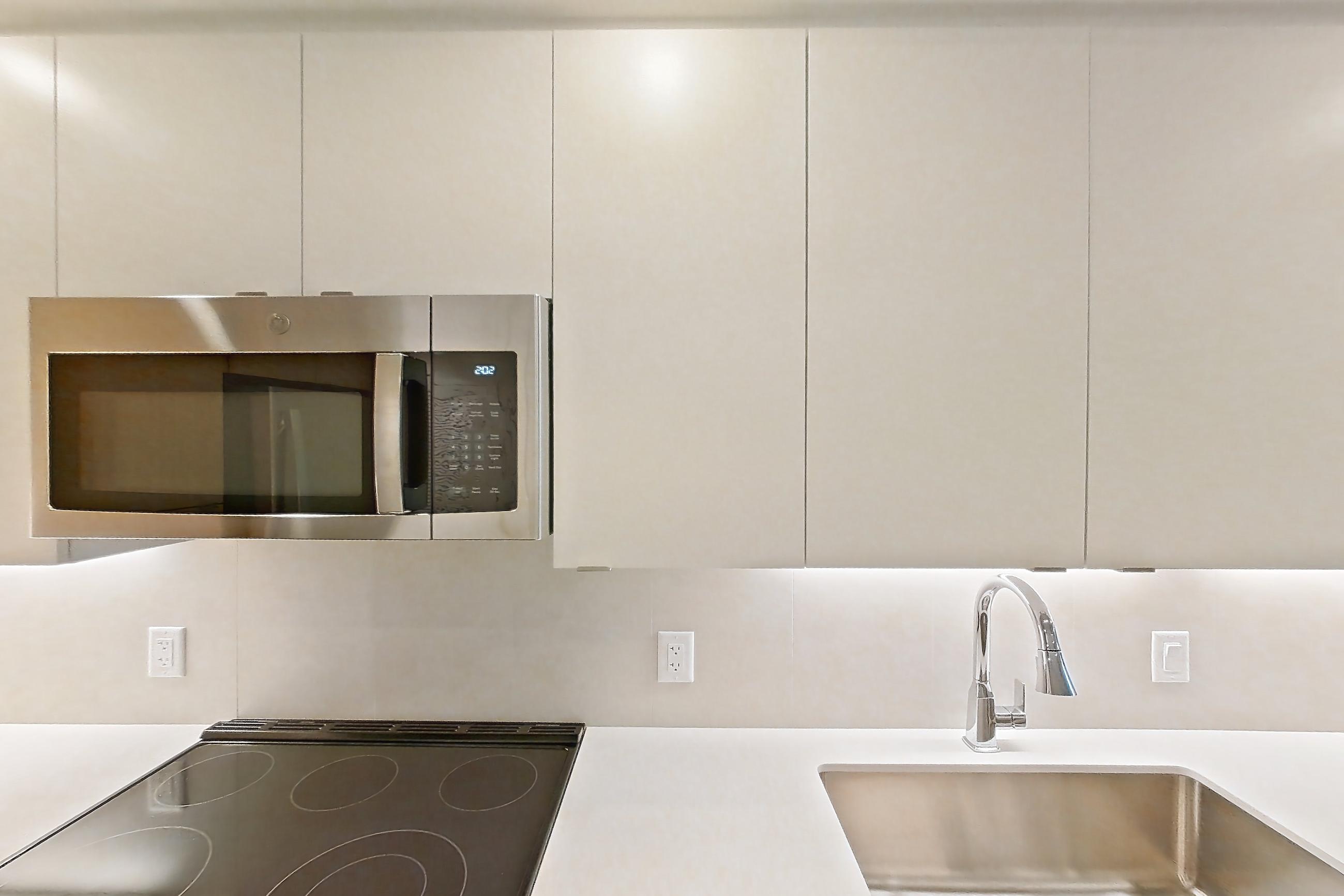 Kitchen with dishwasher, electric range, light countertops, light stone countertops, light wood-finish flooring, microwave, oven/range, refrigerator, and stainless steel appliances, Apartment 111 at Caroline Pompano Beach