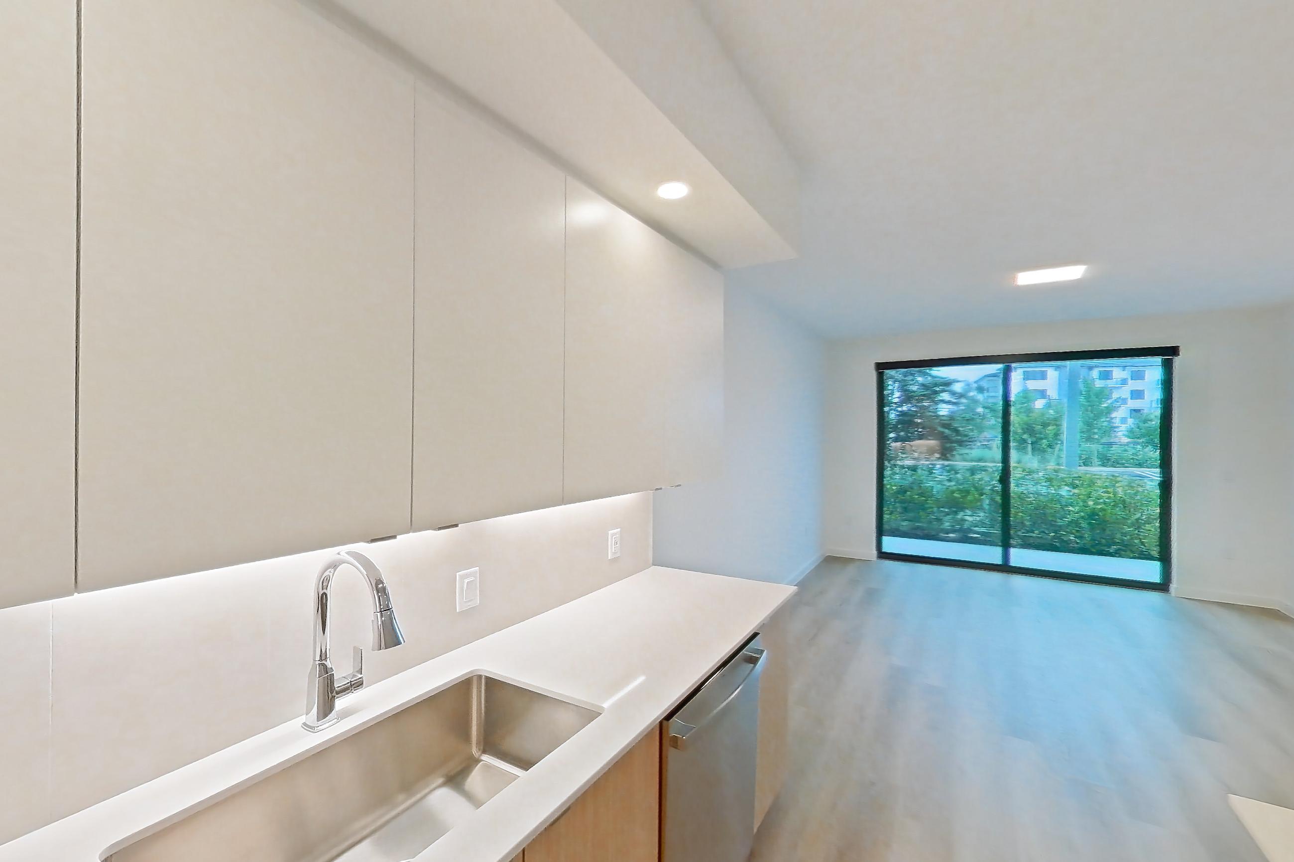 Kitchen with dishwasher, electric range, light countertops, light stone countertops, light wood-finish flooring, microwave, oven/range, refrigerator, and stainless steel appliances, Apartment 111 at Caroline Pompano Beach
