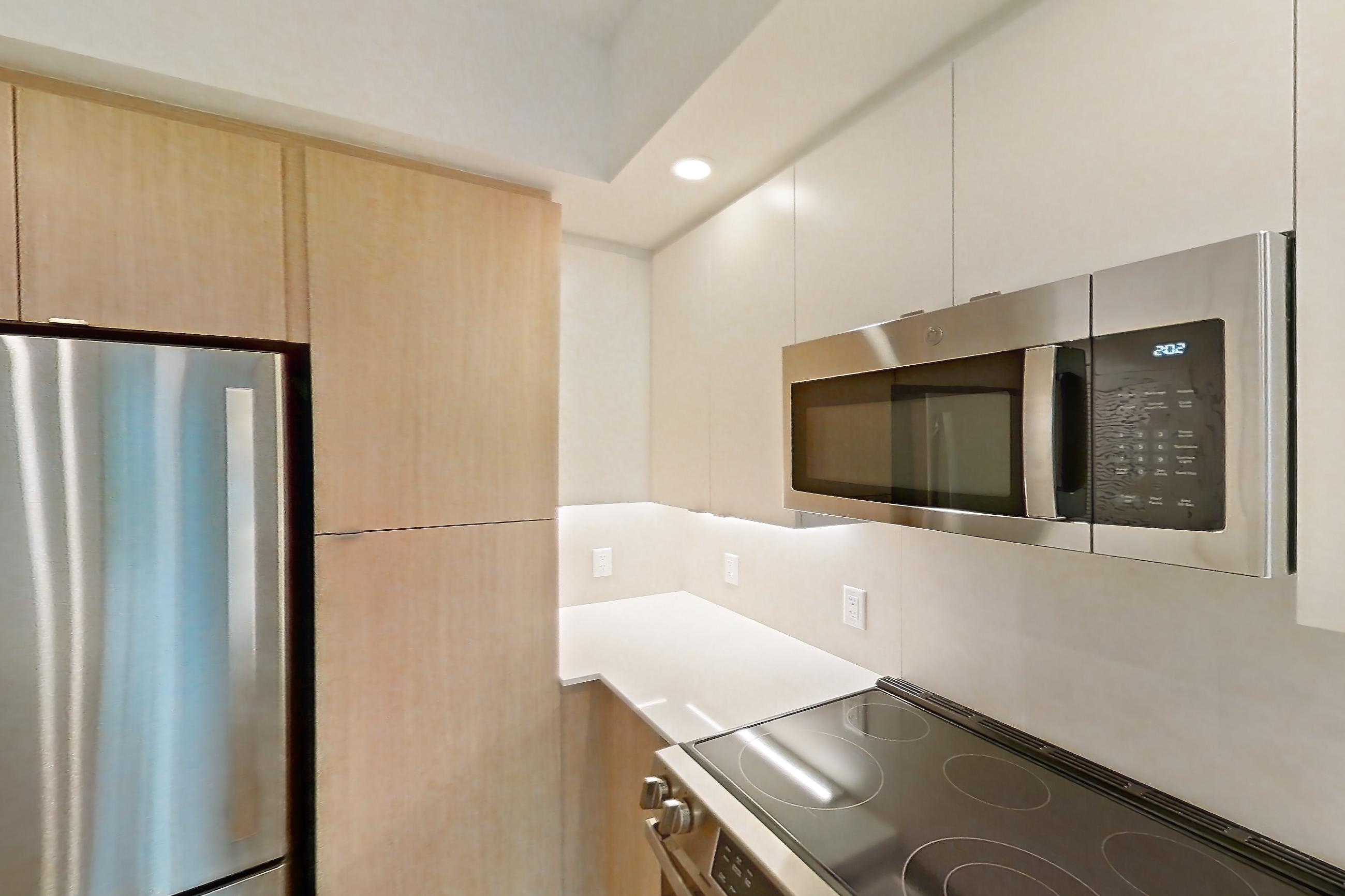 Kitchen with dishwasher, electric range, light countertops, light stone countertops, light wood-finish flooring, microwave, oven/range, refrigerator, and stainless steel appliances, Apartment 111 at Caroline Pompano Beach