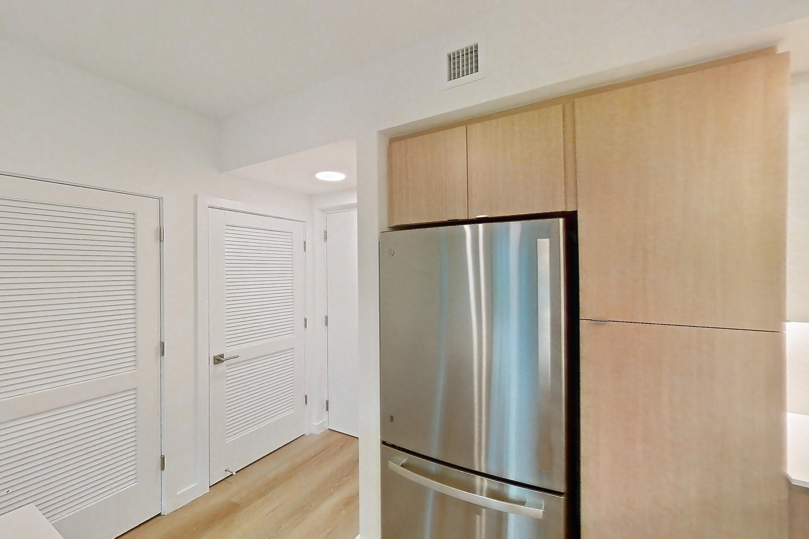 Kitchen with dishwasher, electric range, light countertops, light stone countertops, light wood-finish flooring, microwave, oven/range, refrigerator, and stainless steel appliances, Apartment 111 at Caroline Pompano Beach