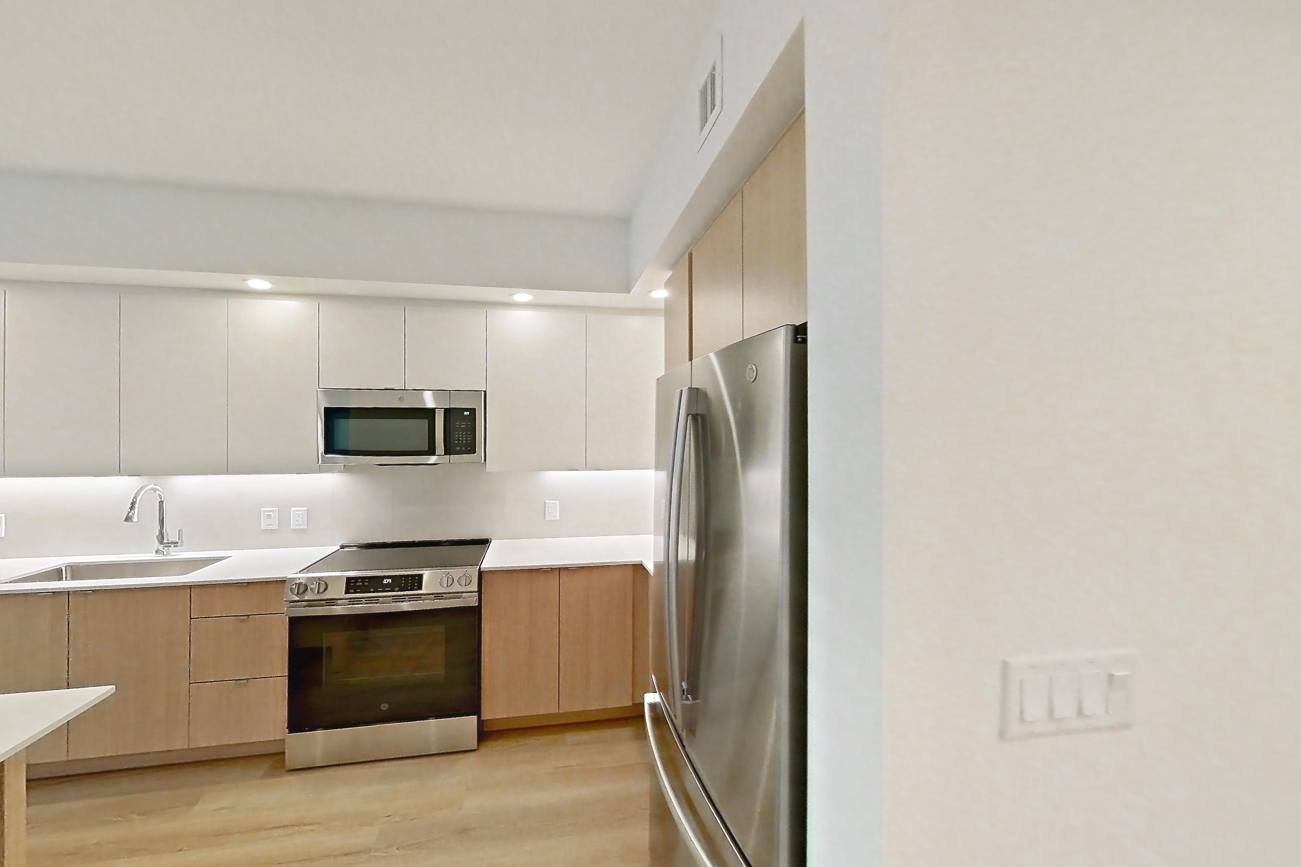 Kitchen entryway with dishwasher, electric range, light countertops, light wood-finish flooring, oven/range, refrigerator, and stainless steel appliances, Apartment 112 at Caroline Pompano Beach