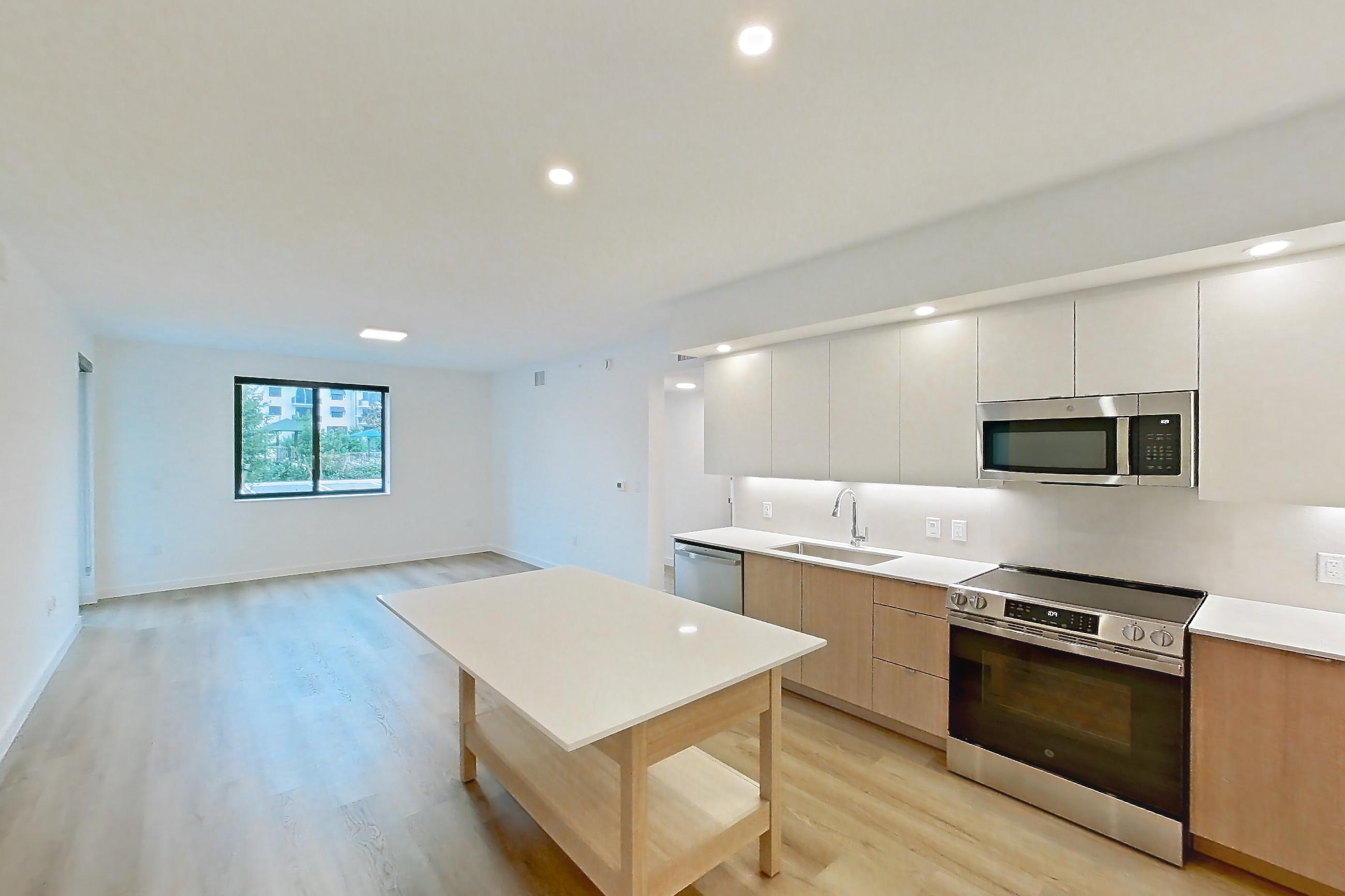 Kitchen entryway with dishwasher, electric range, light countertops, light wood-finish flooring, oven/range, refrigerator, and stainless steel appliances, Apartment 112 at Caroline Pompano Beach