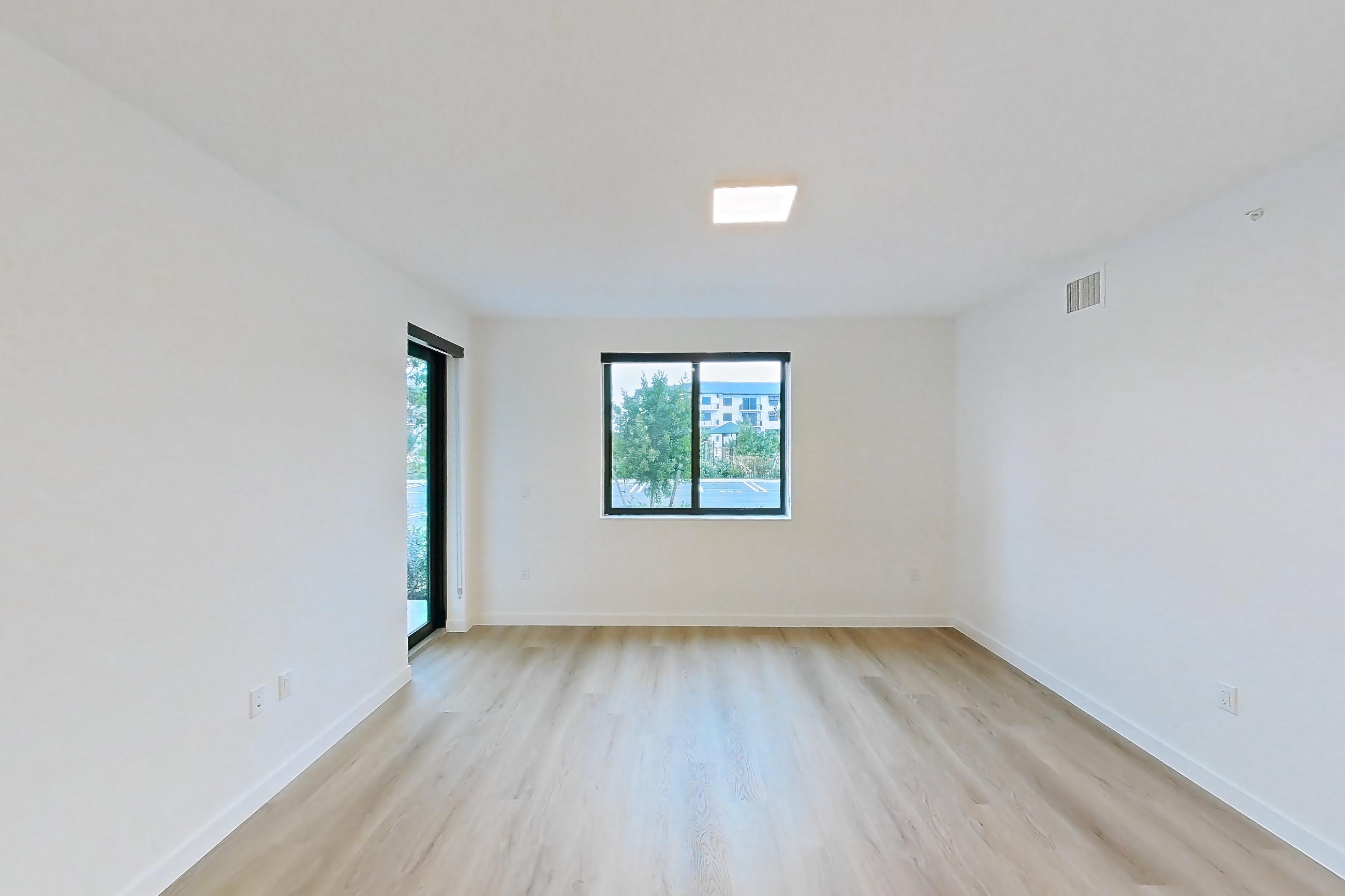 Kitchen island corner with black appliances, dishwasher, electric range, light stone countertops, light wood-finish flooring, oven/range, and stainless steel appliances, Apartment 112 at Caroline Pompano Beach