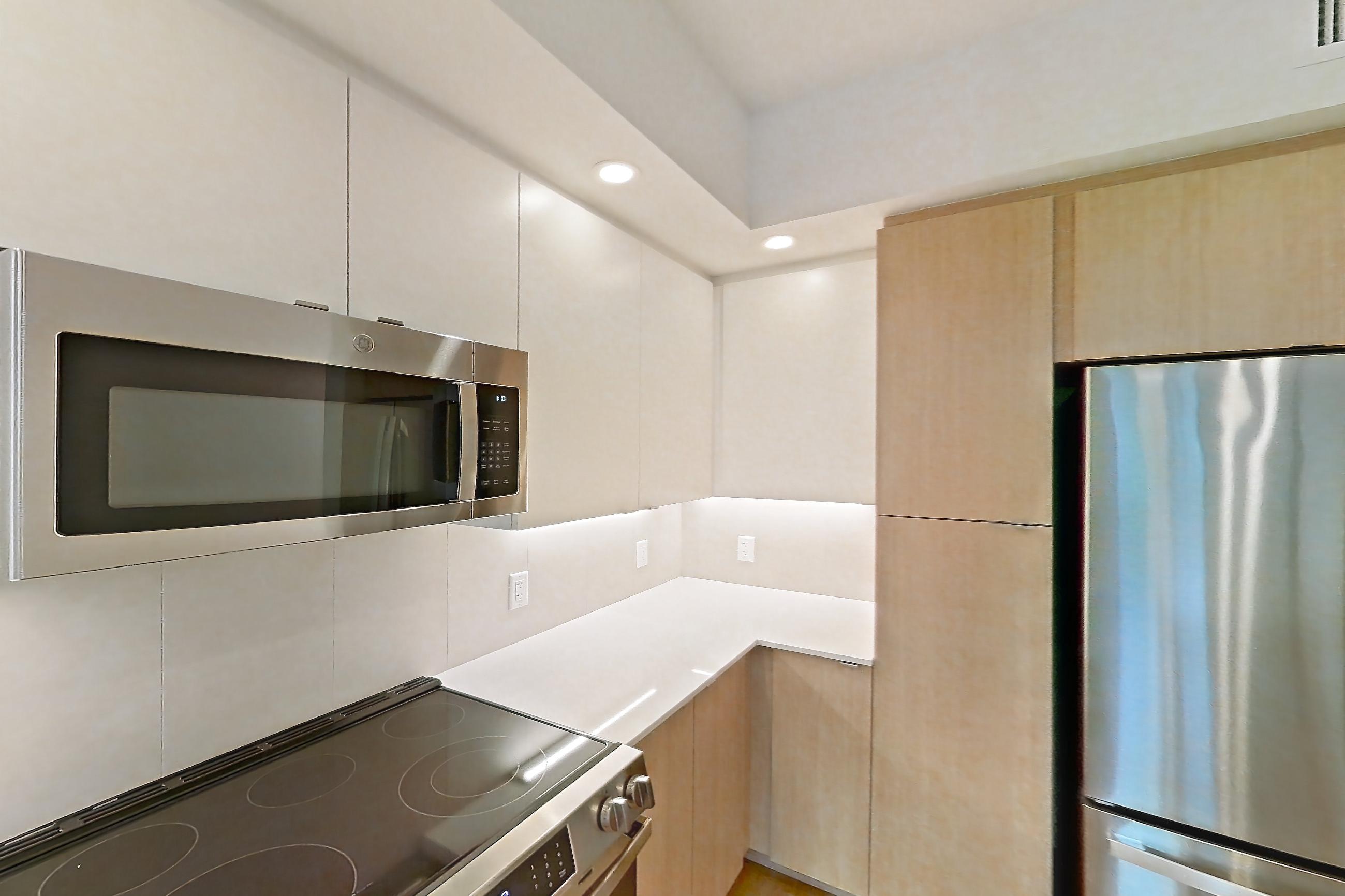 Kitchen with dishwasher, electric range, light countertops, light stone countertops, light wood-finish flooring, microwave, oven/range, refrigerator, and stainless steel appliances, Apartment 112 at Caroline Pompano Beach