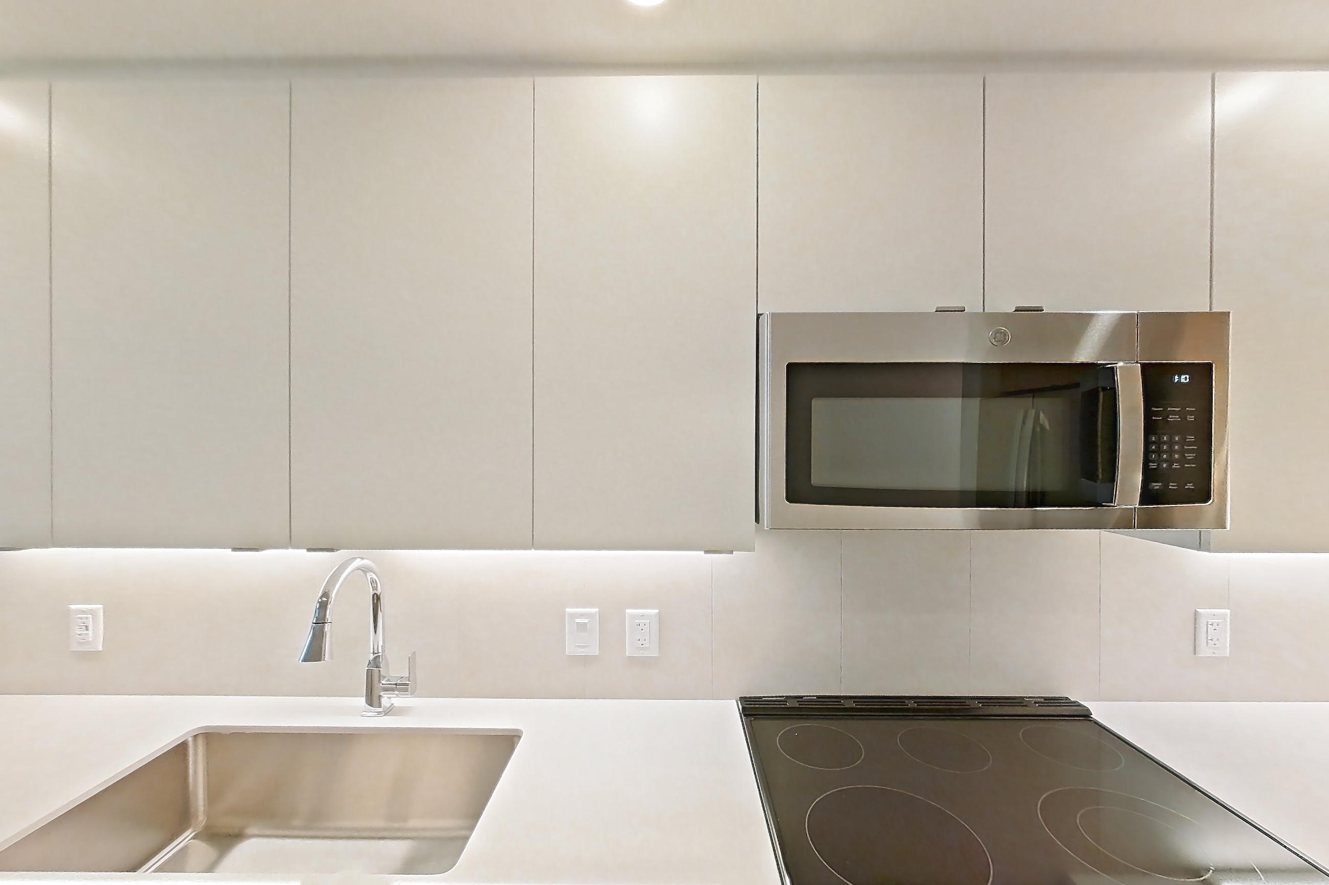 Kitchen with dishwasher, electric range, light countertops, light stone countertops, light wood-finish flooring, microwave, oven/range, refrigerator, and stainless steel appliances, Apartment 112 at Caroline Pompano Beach