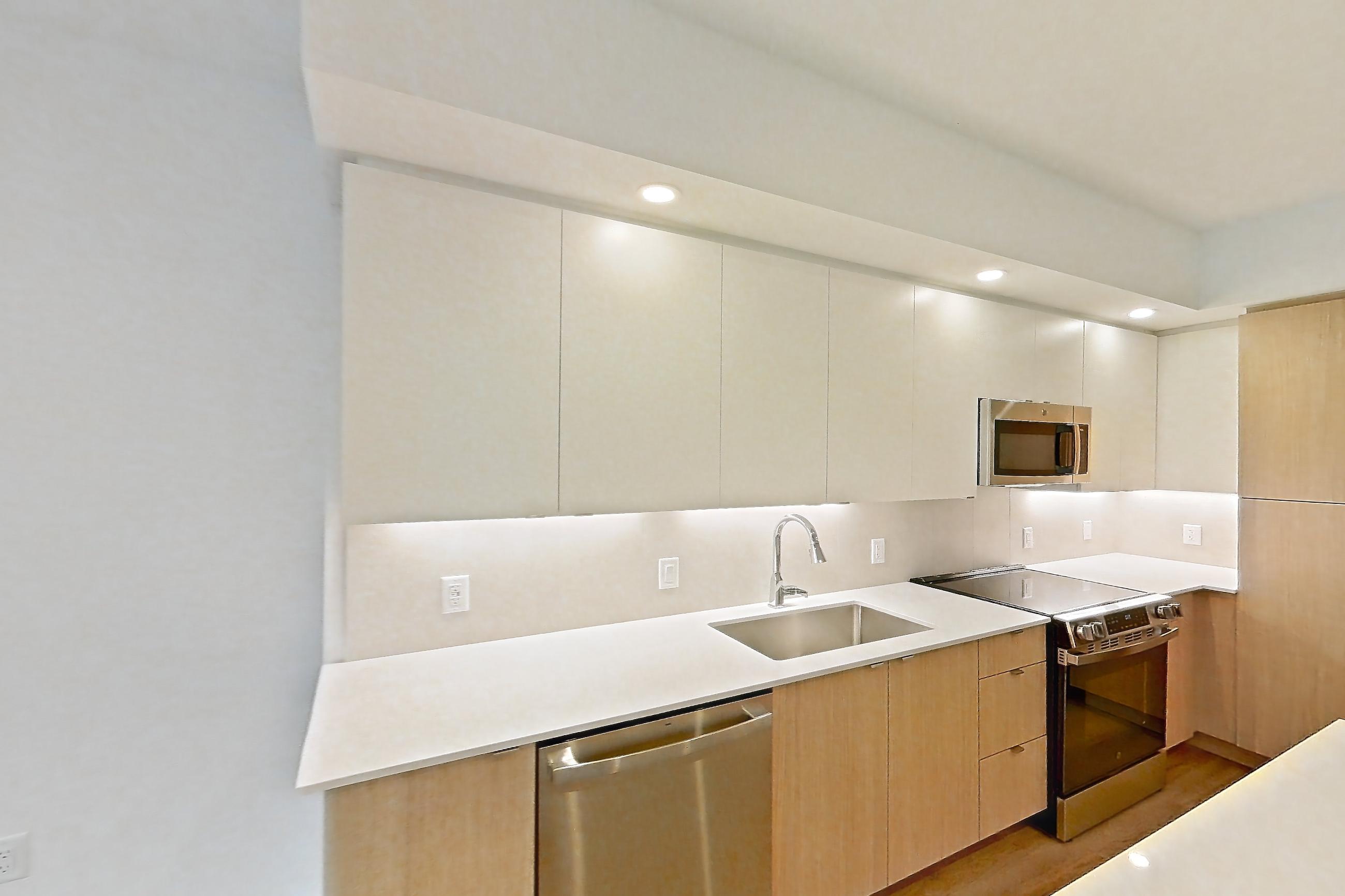 Kitchen island corner with dishwasher, light stone countertops, light wood-finish flooring, and stainless steel appliances, Apartment 201 at Caroline Pompano Beach