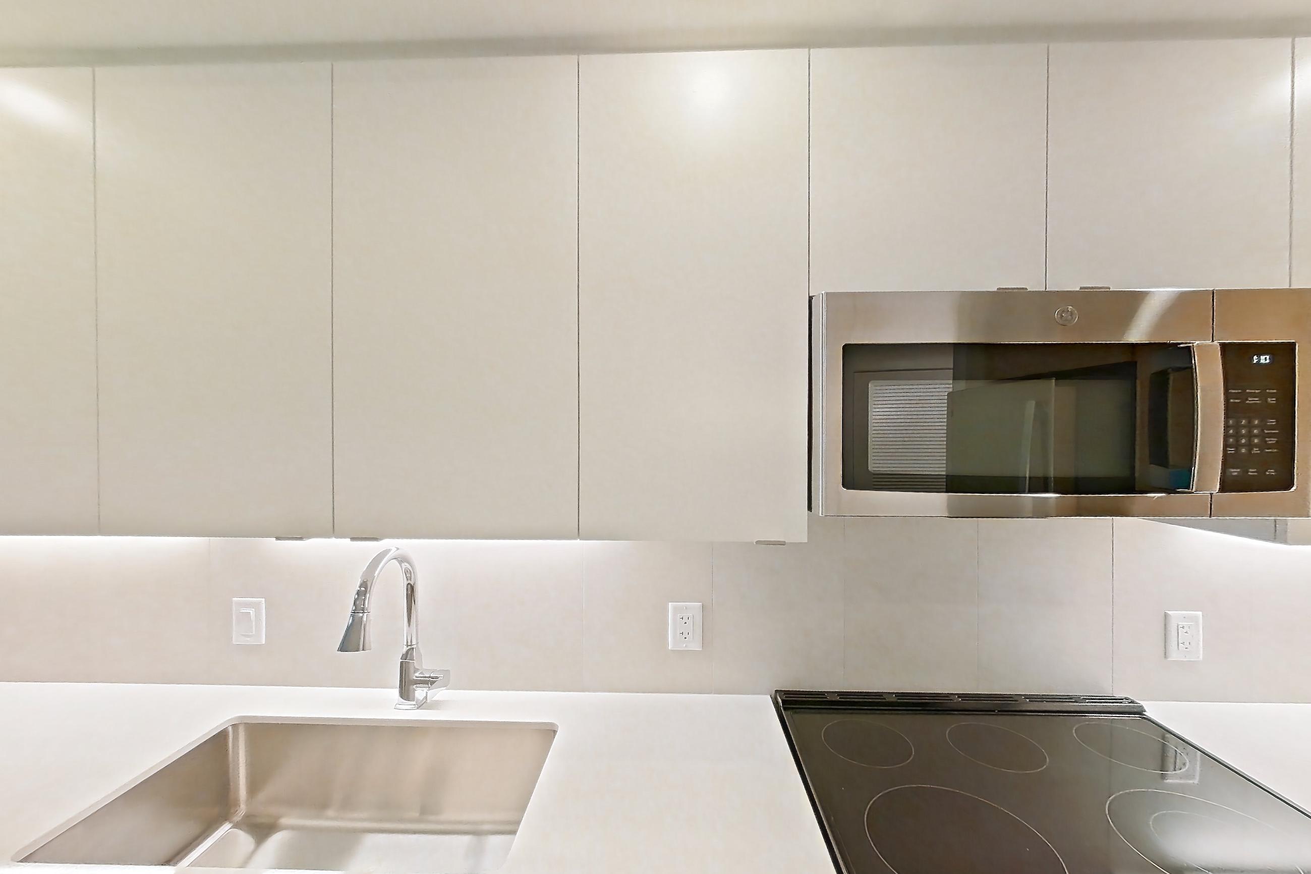 Kitchen with dishwasher, electric range, light countertops, light stone countertops, light wood-finish flooring, microwave, oven/range, refrigerator, and stainless steel appliances, Apartment 201 at Caroline Pompano Beach