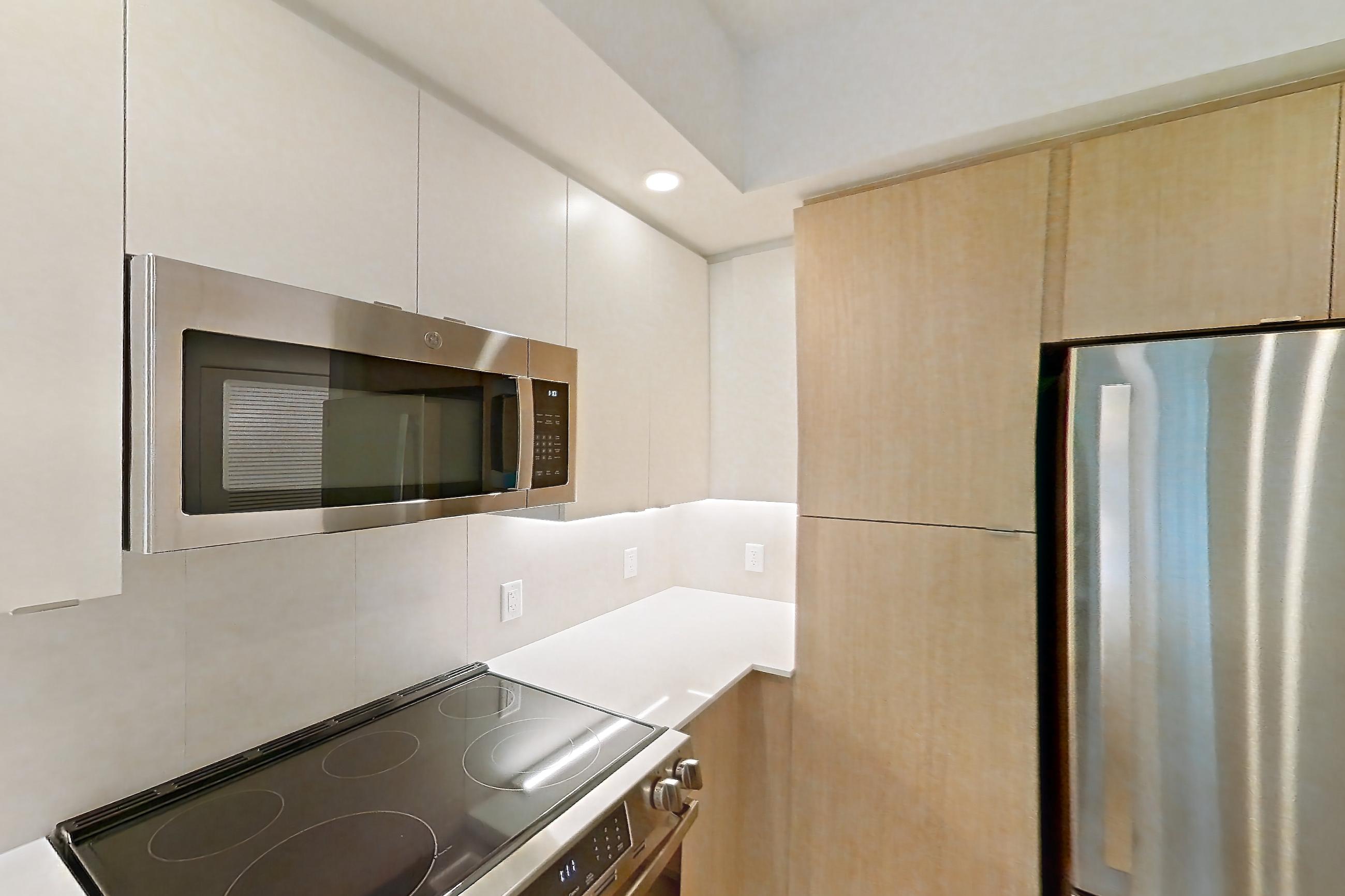 Kitchen with dishwasher, electric range, light countertops, light stone countertops, light wood-finish flooring, microwave, oven/range, refrigerator, and stainless steel appliances, Apartment 201 at Caroline Pompano Beach