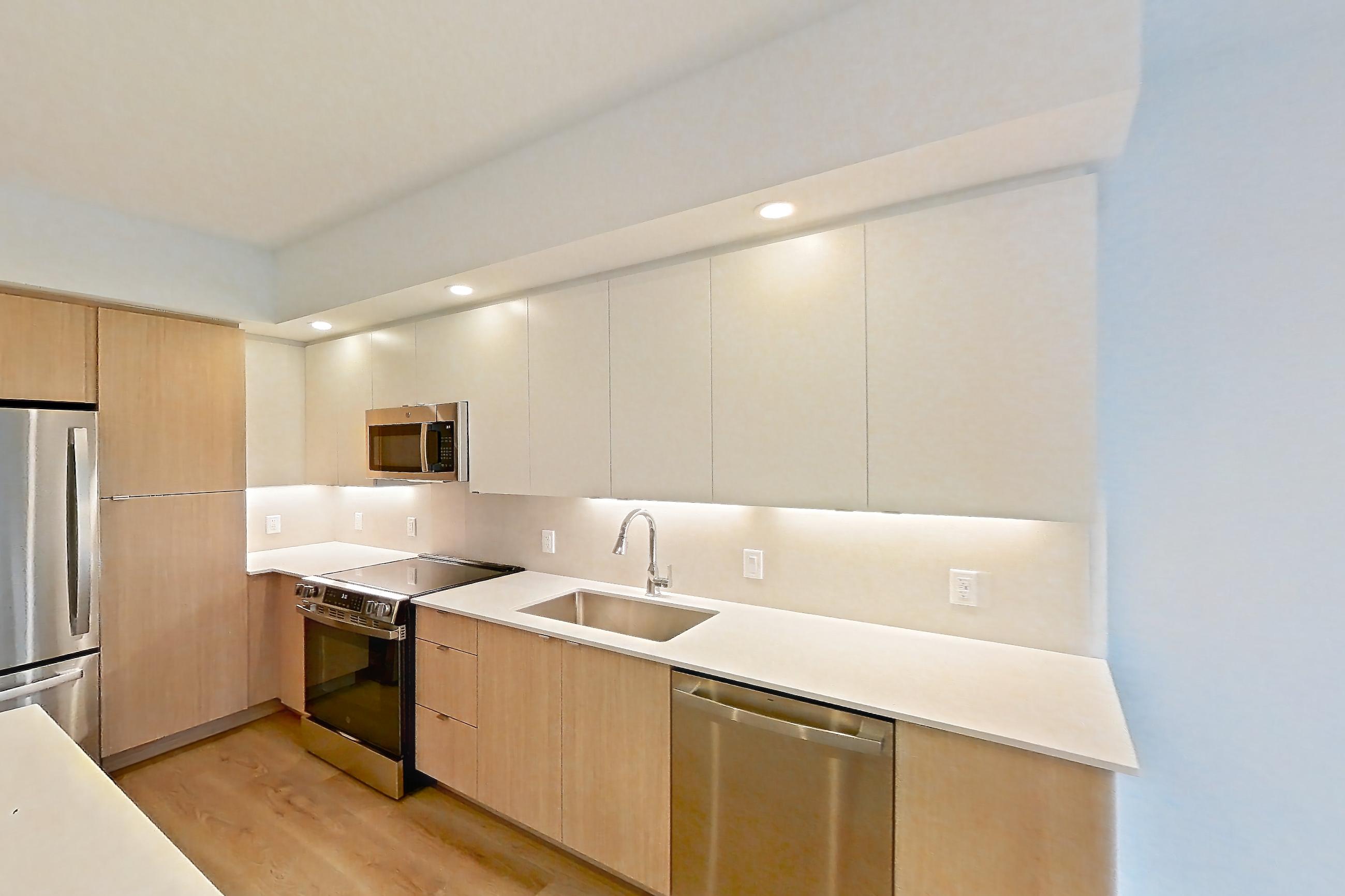 Kitchen island corner with dishwasher, light stone countertops, light wood-finish flooring, and stainless steel appliances, Apartment 205 at Caroline Pompano Beach
