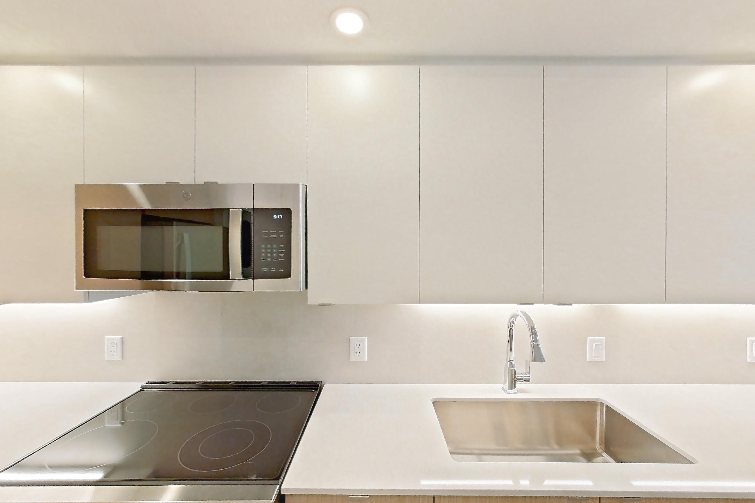 Kitchen with dishwasher, electric range, light countertops, light wood-finish flooring, microwave, oven/range, refrigerator, and stainless steel appliances, Apartment 205 at Caroline Pompano Beach