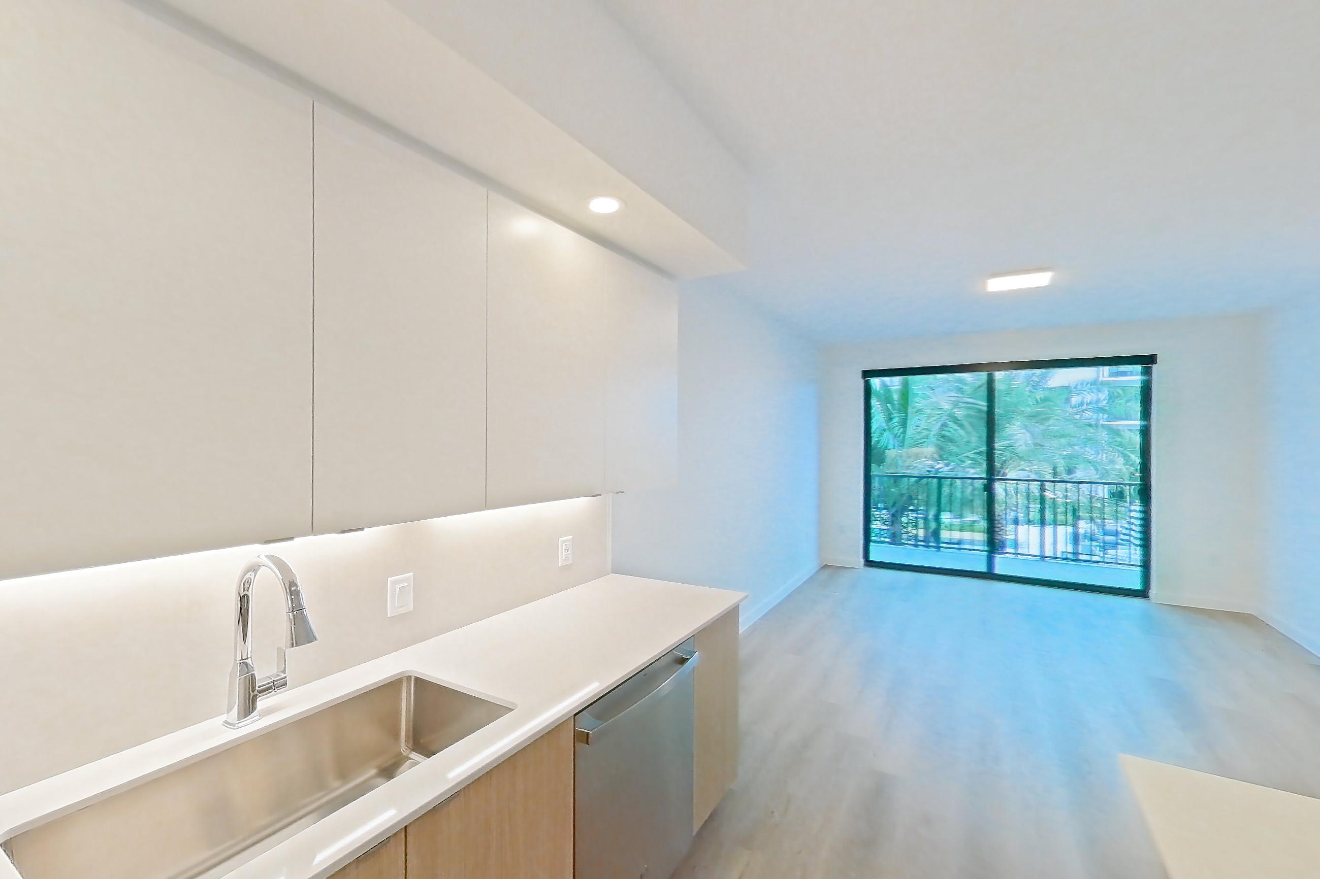 Kitchen with dishwasher, electric range, light countertops, light wood-finish flooring, microwave, oven/range, refrigerator, and stainless steel appliances, Apartment 205 at Caroline Pompano Beach