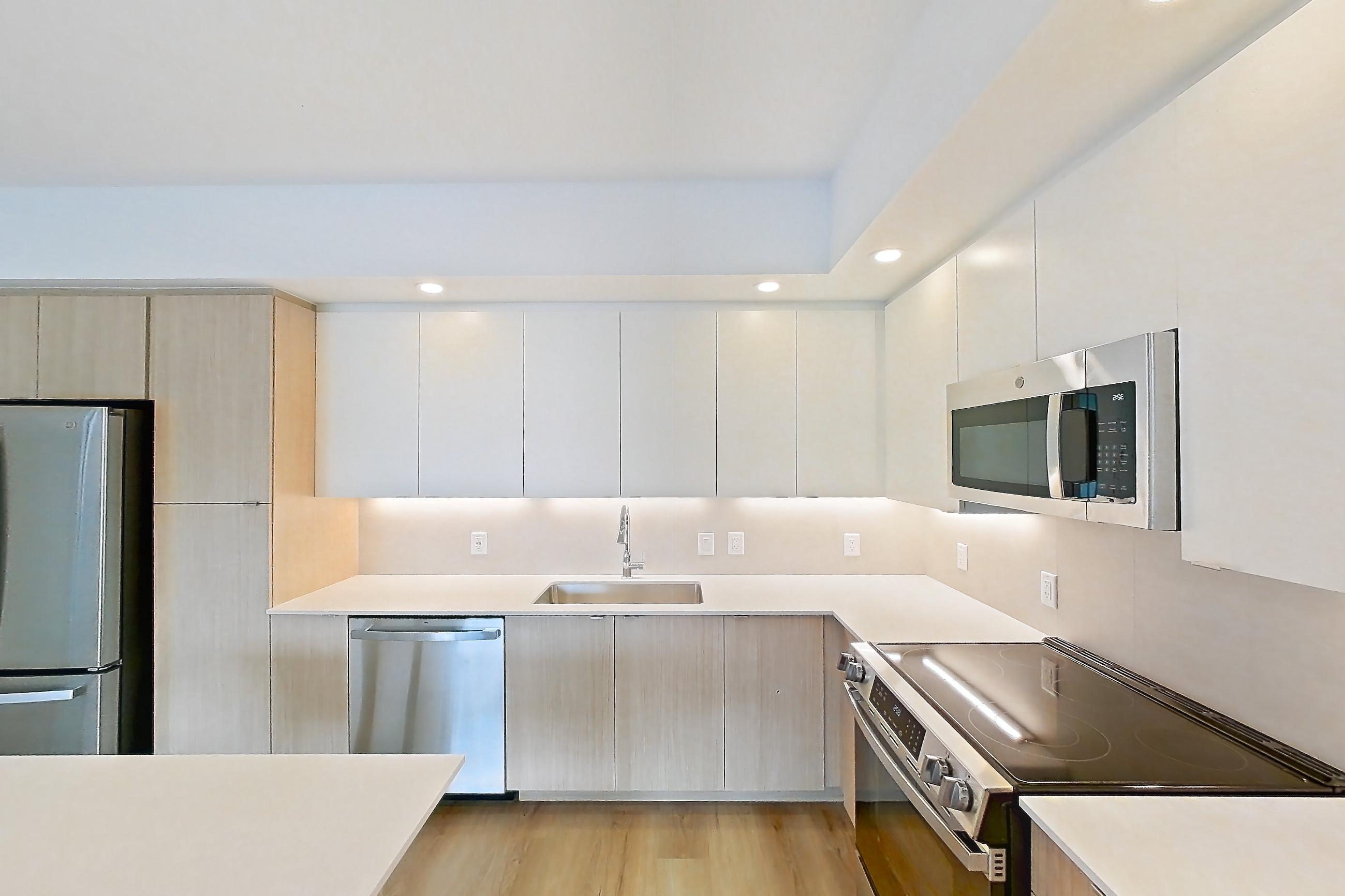 Kitchen island corner with black appliances, electric range, light countertops, light wood-finish flooring, oven/range, refrigerator, and stainless steel appliances, Apartment 208 at Caroline Pompano Beach