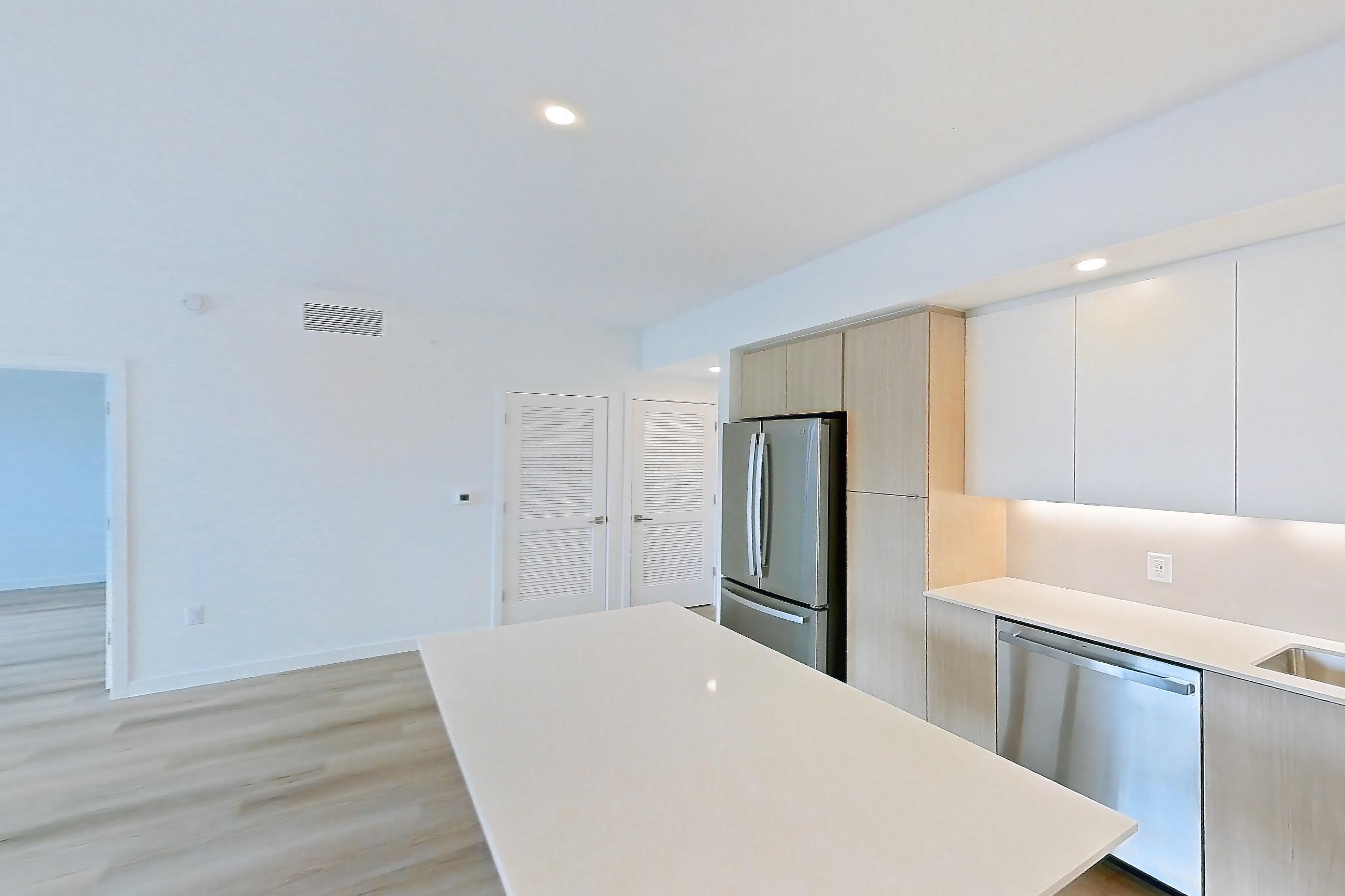 Kitchen island corner with black appliances, electric range, light countertops, light wood-finish flooring, oven/range, refrigerator, and stainless steel appliances, Apartment 208 at Caroline Pompano Beach