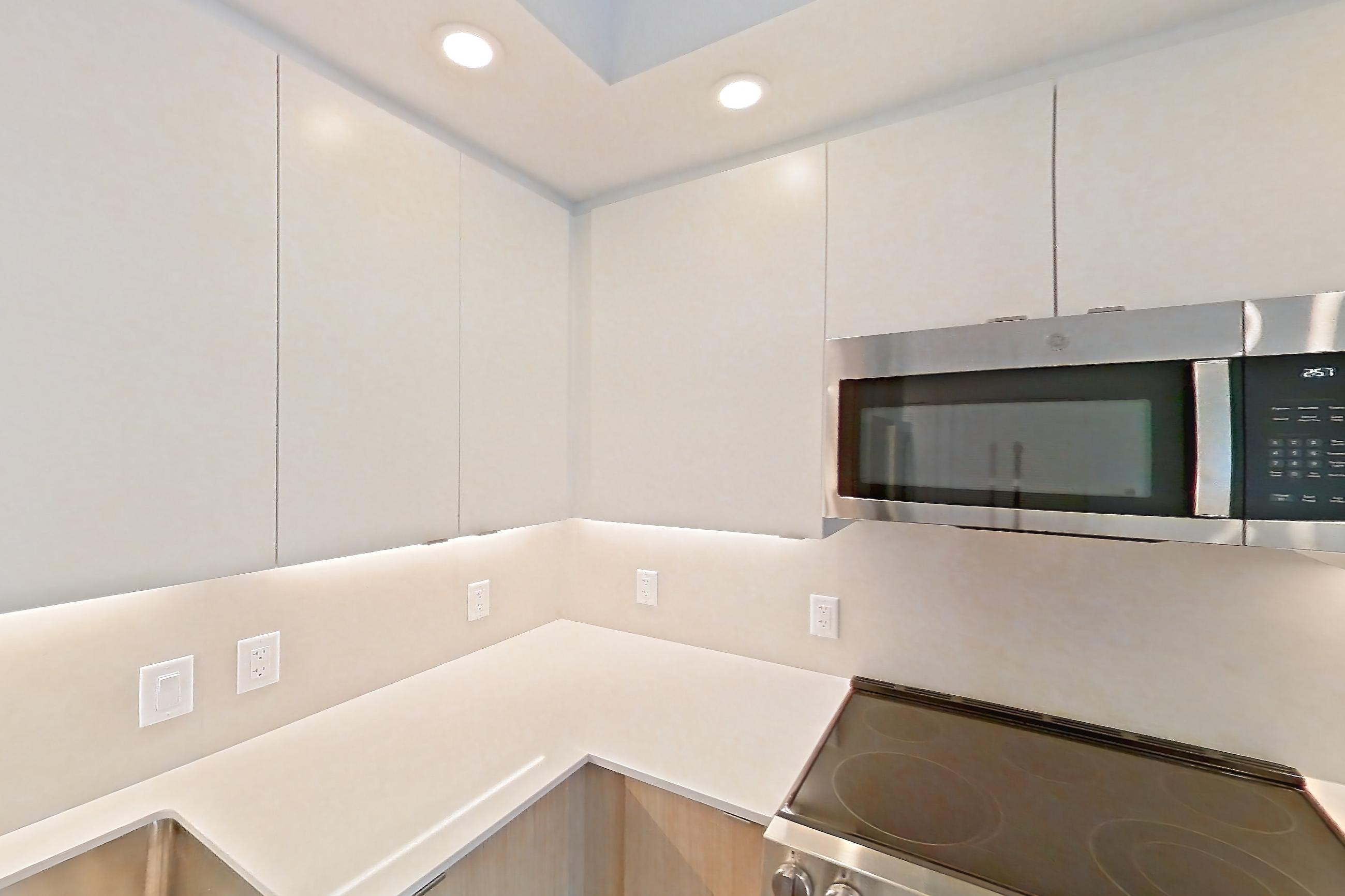 Kitchen with dishwasher, electric range, light countertops, light stone countertops, light wood-finish flooring, microwave, oven/range, refrigerator, and stainless steel appliances, Apartment 208 at Caroline Pompano Beach