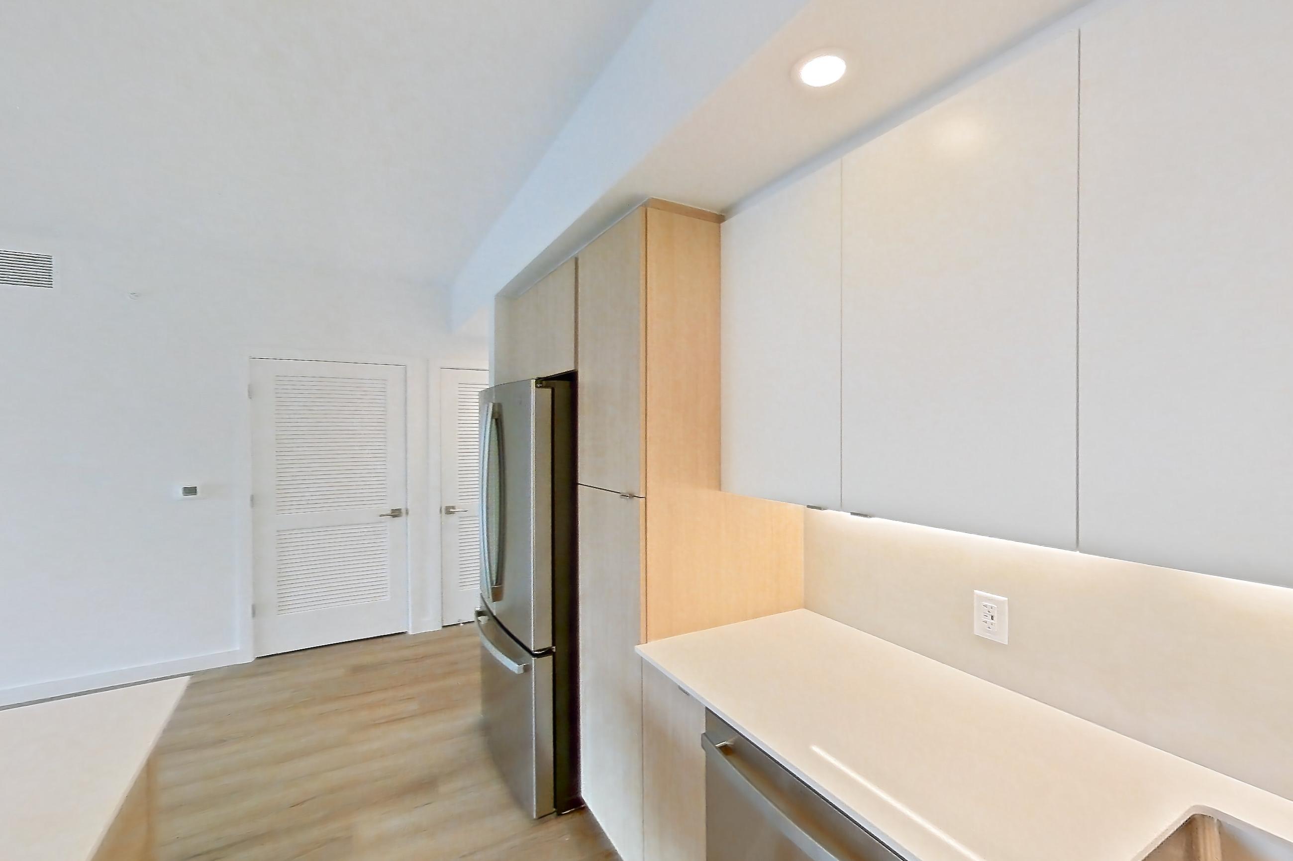 Kitchen with dishwasher, electric range, light countertops, light stone countertops, light wood-finish flooring, microwave, oven/range, refrigerator, and stainless steel appliances, Apartment 208 at Caroline Pompano Beach