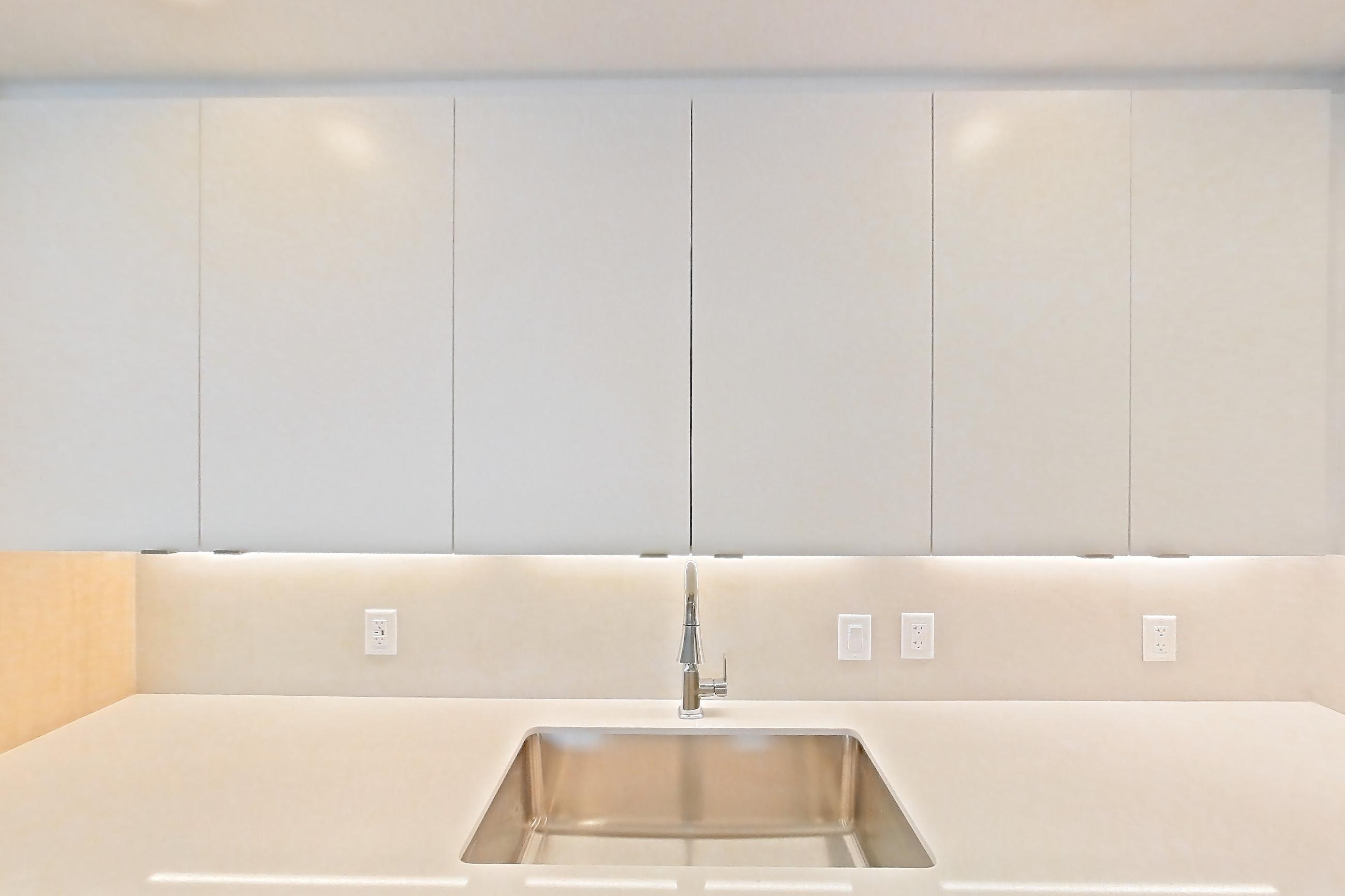 Kitchen with dishwasher, electric range, light countertops, light stone countertops, light wood-finish flooring, microwave, oven/range, refrigerator, and stainless steel appliances, Apartment 208 at Caroline Pompano Beach