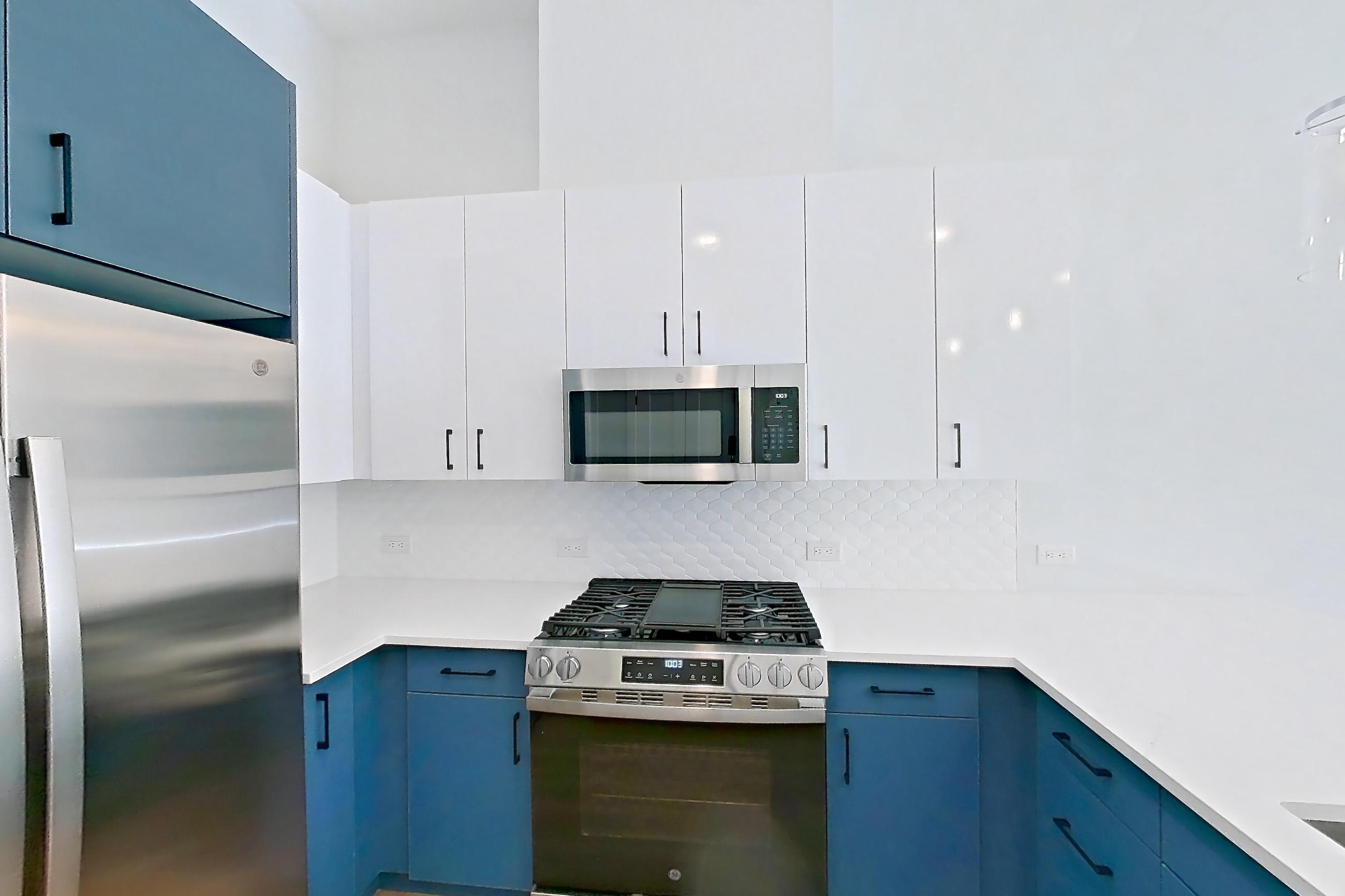 Kitchen with dishwasher, gas range, kitchen island, light countertops, light stone countertops, light wood-finish flooring, microwave, oven/range, refrigerator, stainless steel appliances, and water & ice dispenser, Apartment 116 at Bria