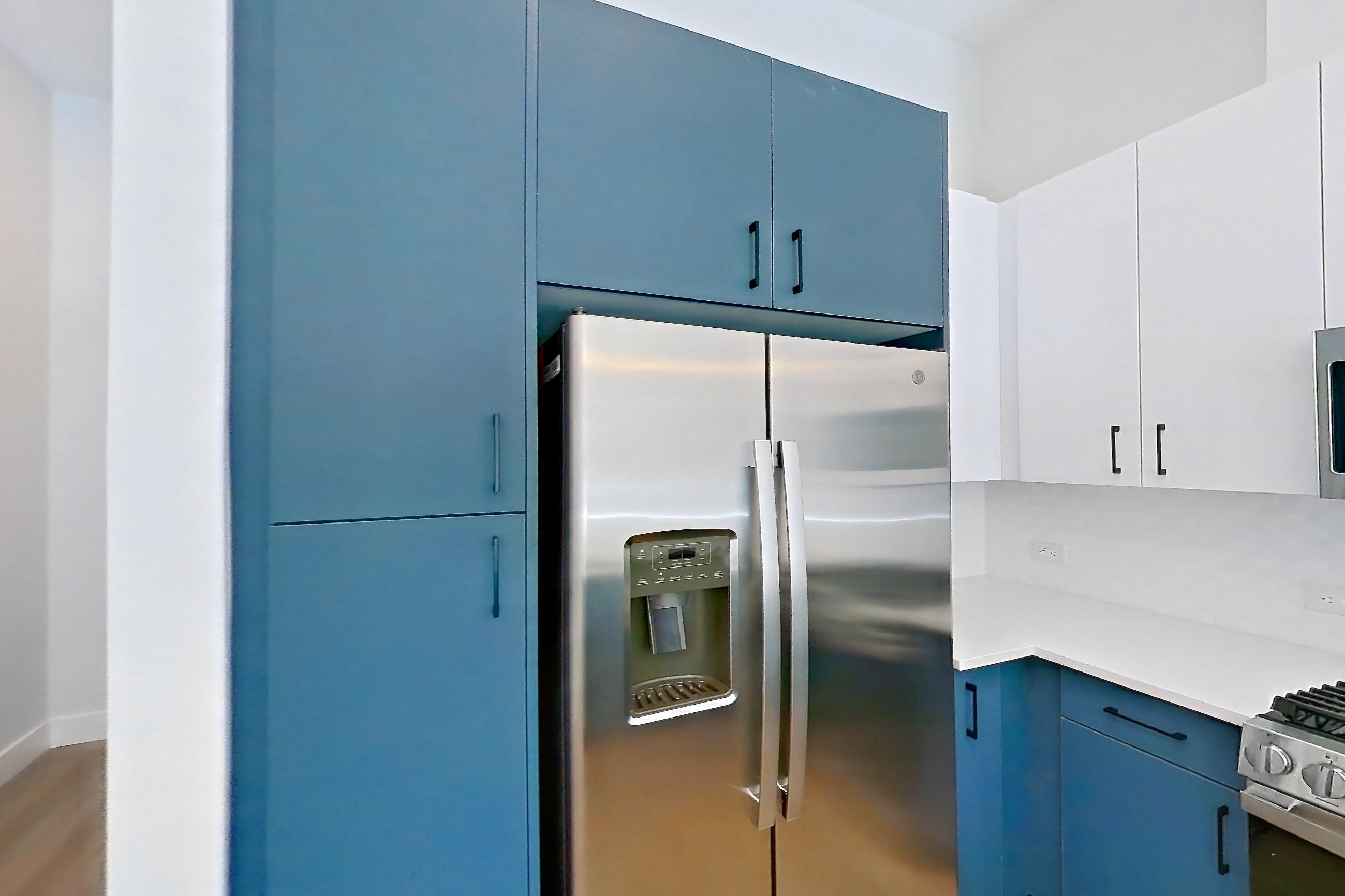 Kitchen with dishwasher, gas range, kitchen island, light countertops, light stone countertops, light wood-finish flooring, microwave, oven/range, refrigerator, stainless steel appliances, and water & ice dispenser, Apartment 116 at Bria