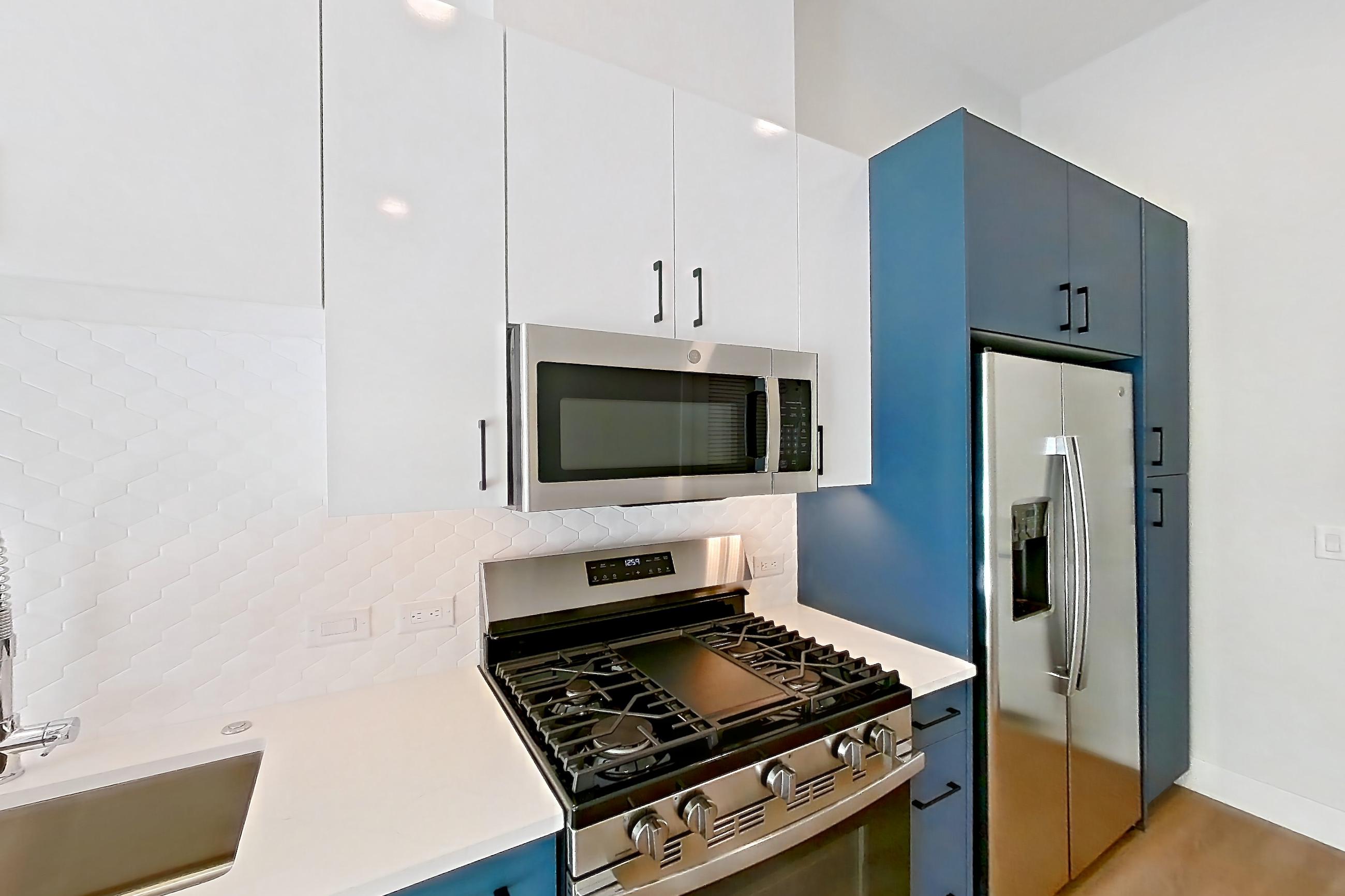 Kitchen with gas range, light countertops, light stone countertops, light wood-finish flooring, microwave, oven/range, refrigerator, stainless steel appliances, and water & ice dispenser, Apartment 122 at Bria