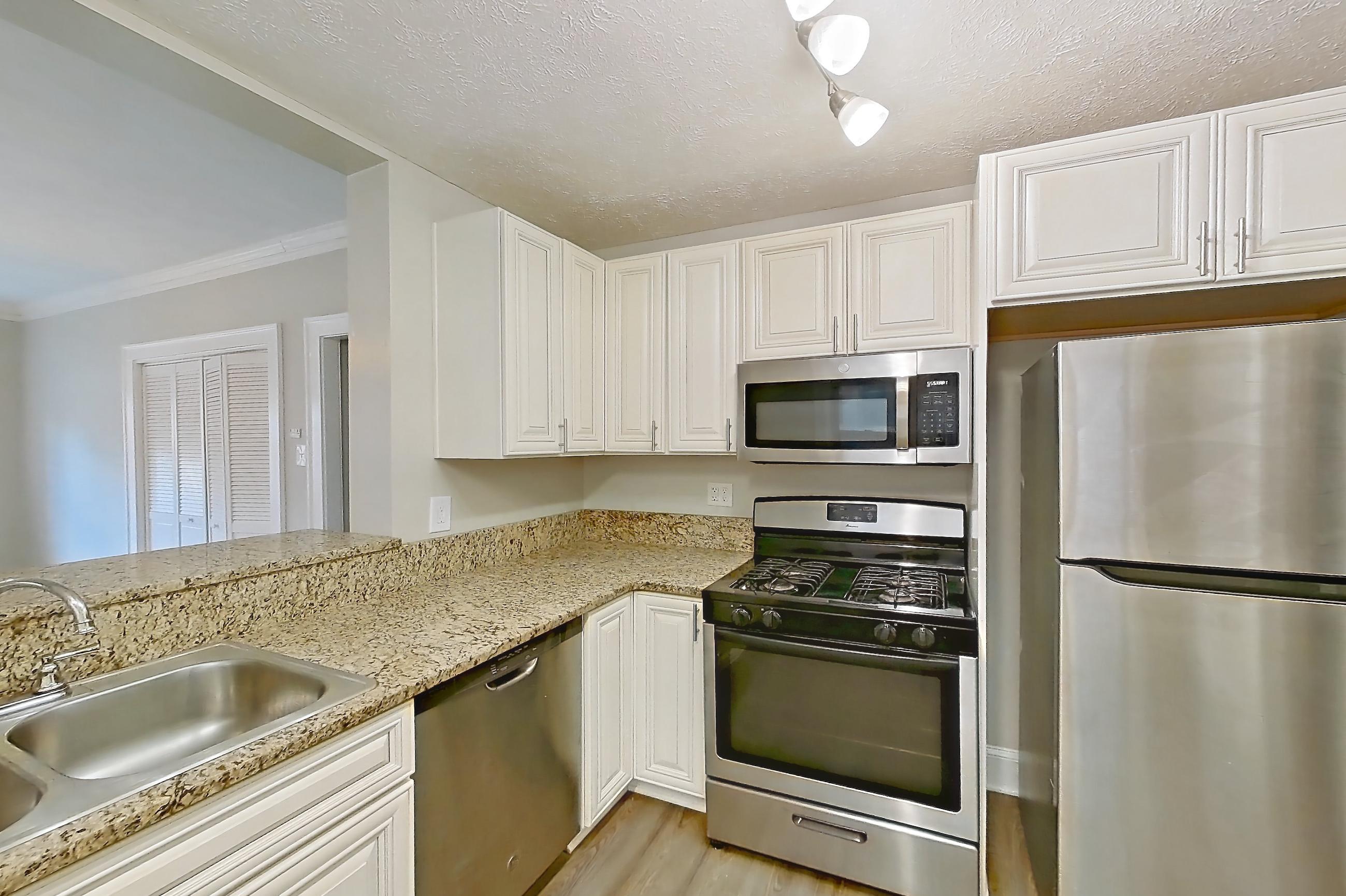 Kitchen with dark wood-finish flooring, dishwasher, gas range, light countertops, light stone countertops, light wood-finish flooring, microwave, oven/range, radiator heat, refrigerator, and stainless steel appliances, Apartment MVI-01 at Mapleview