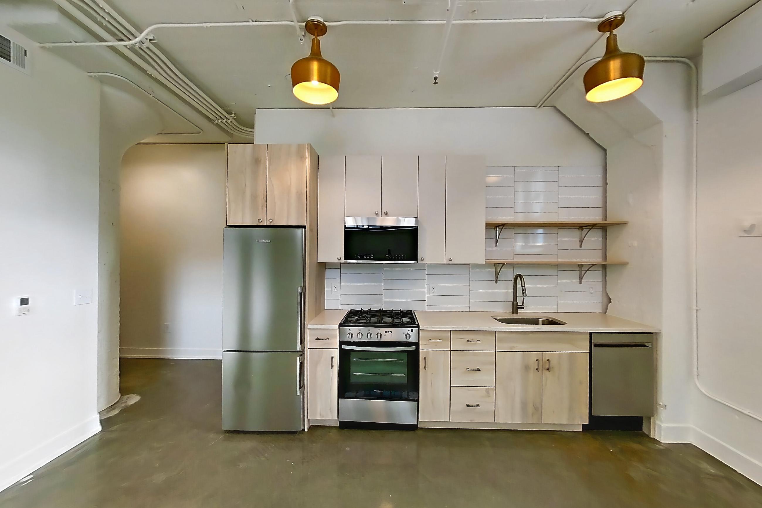 Living room and kitchen with dark concrete flooring, dishwasher, gas range, light countertops, mini-split AC, oven/range, polished concrete flooring, refrigerator, and stainless steel appliances, Apartment 207 at The Hall Lofts