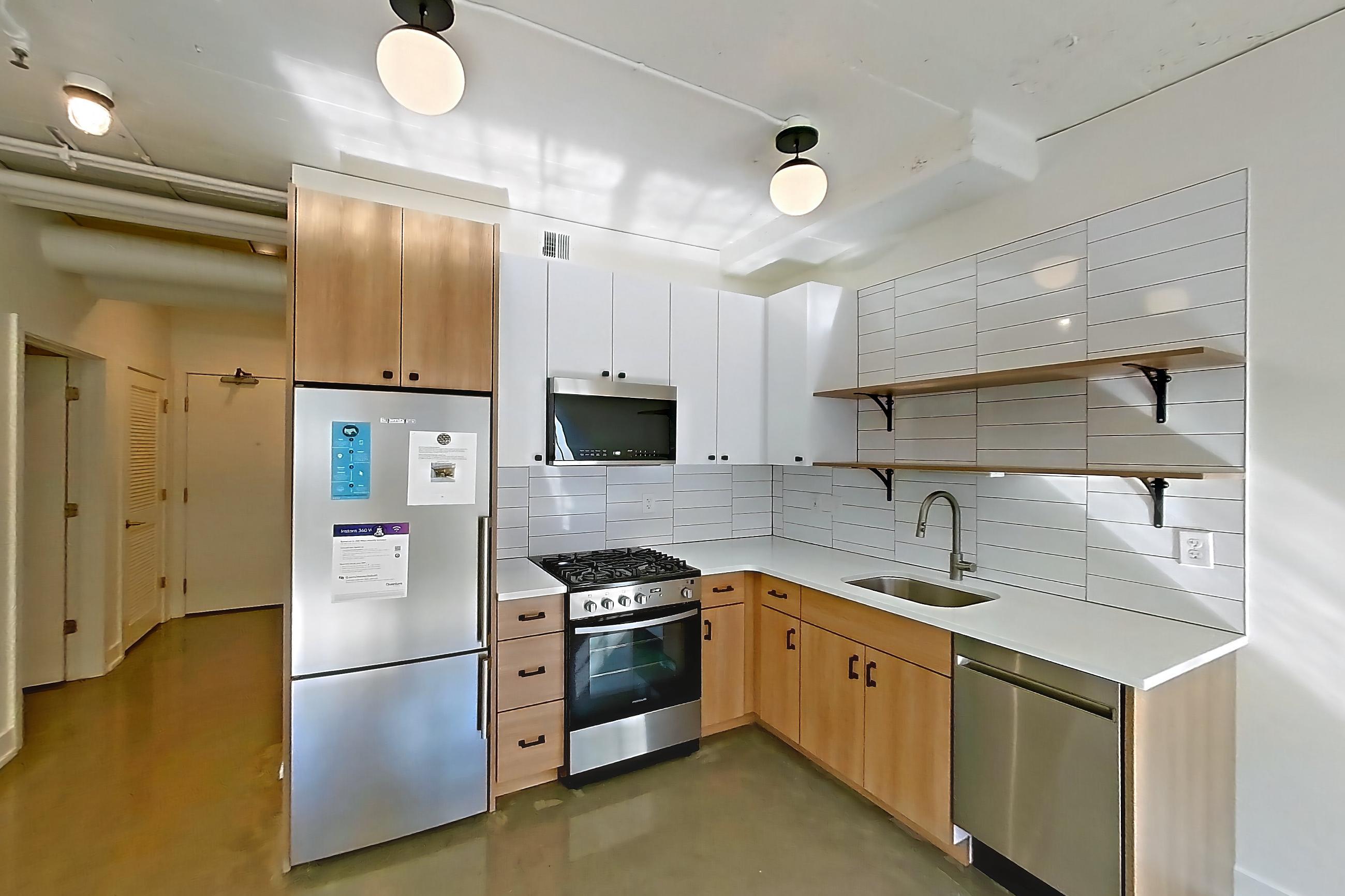 Living room and kitchen with dark concrete flooring, dishwasher, gas range, light countertops, light stone countertops, mini-split AC, oven/range, polished concrete flooring, refrigerator, and stainless steel appliances, Apartment 341 at The Hall Lofts