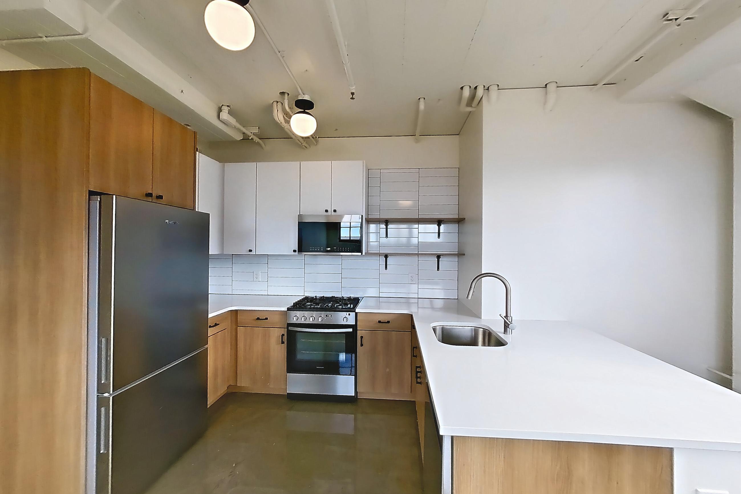 Living room and kitchen with dark concrete flooring, gas range, light stone countertops, mini-split AC, oven/range, polished concrete flooring, refrigerator, skyline view, and stainless steel appliances, Apartment 747 at The Hall Lofts
