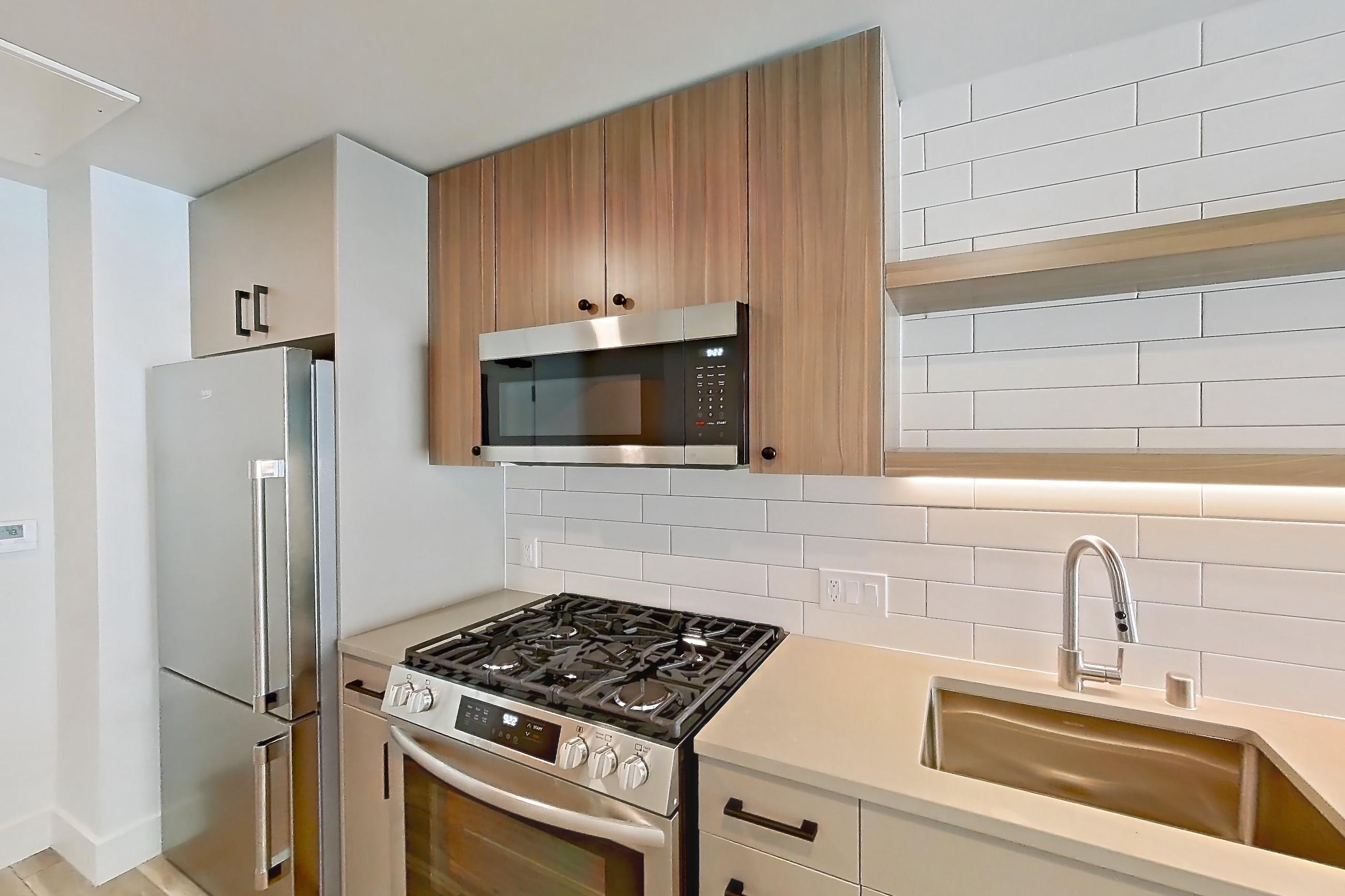 Kitchen with dishwasher, gas range, light countertops, light wood-finish flooring, oven/range, refrigerator, and stainless steel appliances, Apartment 209 at The Myles