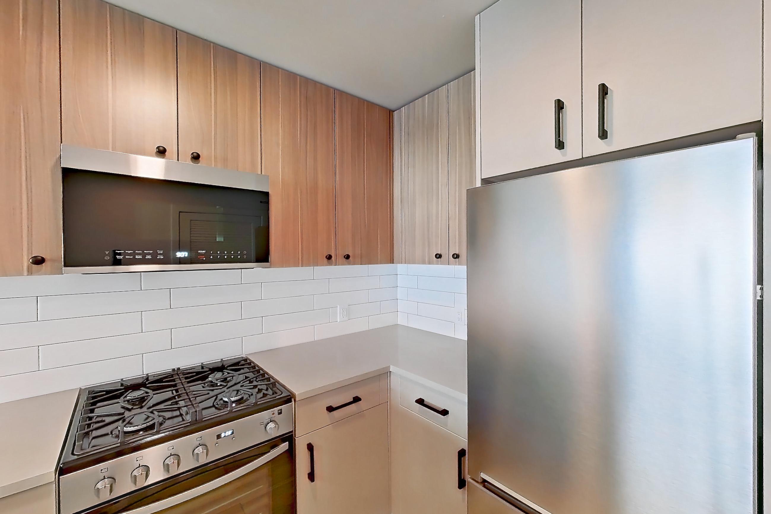 Kitchen with gas range, light countertops, light wood-finish flooring, oven/range, refrigerator, and stainless steel appliances, Apartment 210 at The Myles