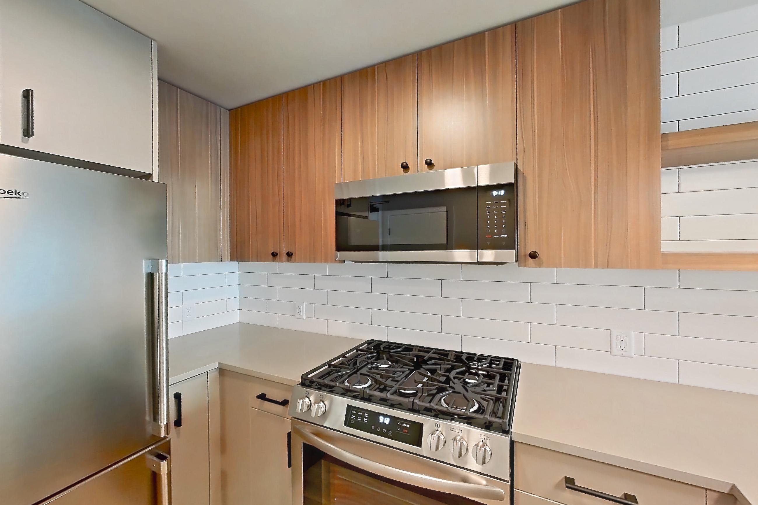 Kitchen with dishwasher, gas range, light countertops, light wood-finish flooring, microwave, oven/range, refrigerator, stainless steel appliances, and wood-look tile flooring, Apartment 214 at The Myles