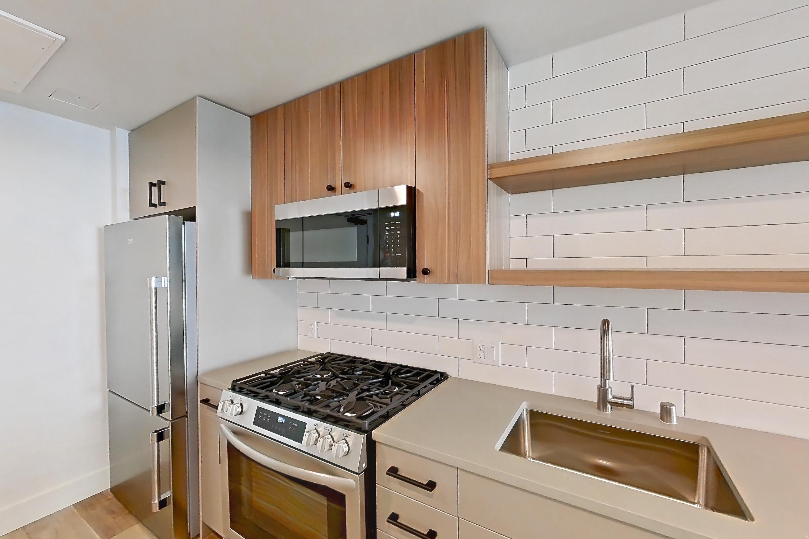 Kitchen with dishwasher, gas range, light countertops, light wood-finish flooring, microwave, oven/range, refrigerator, and stainless steel appliances, Apartment 216 at The Myles