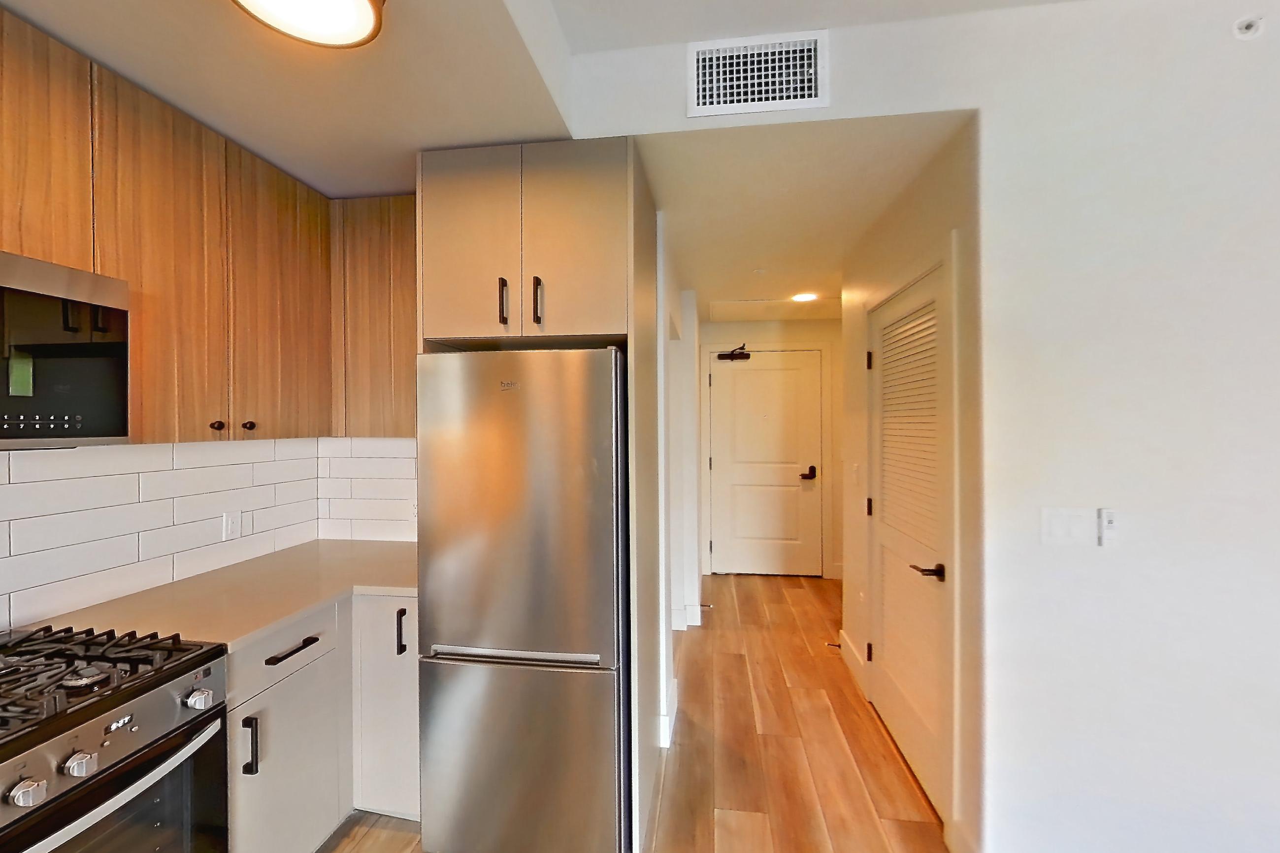 Kitchen with dishwasher, gas range, light countertops, light wood-finish flooring, oven/range, refrigerator, and stainless steel appliances, Apartment 220 at The Myles