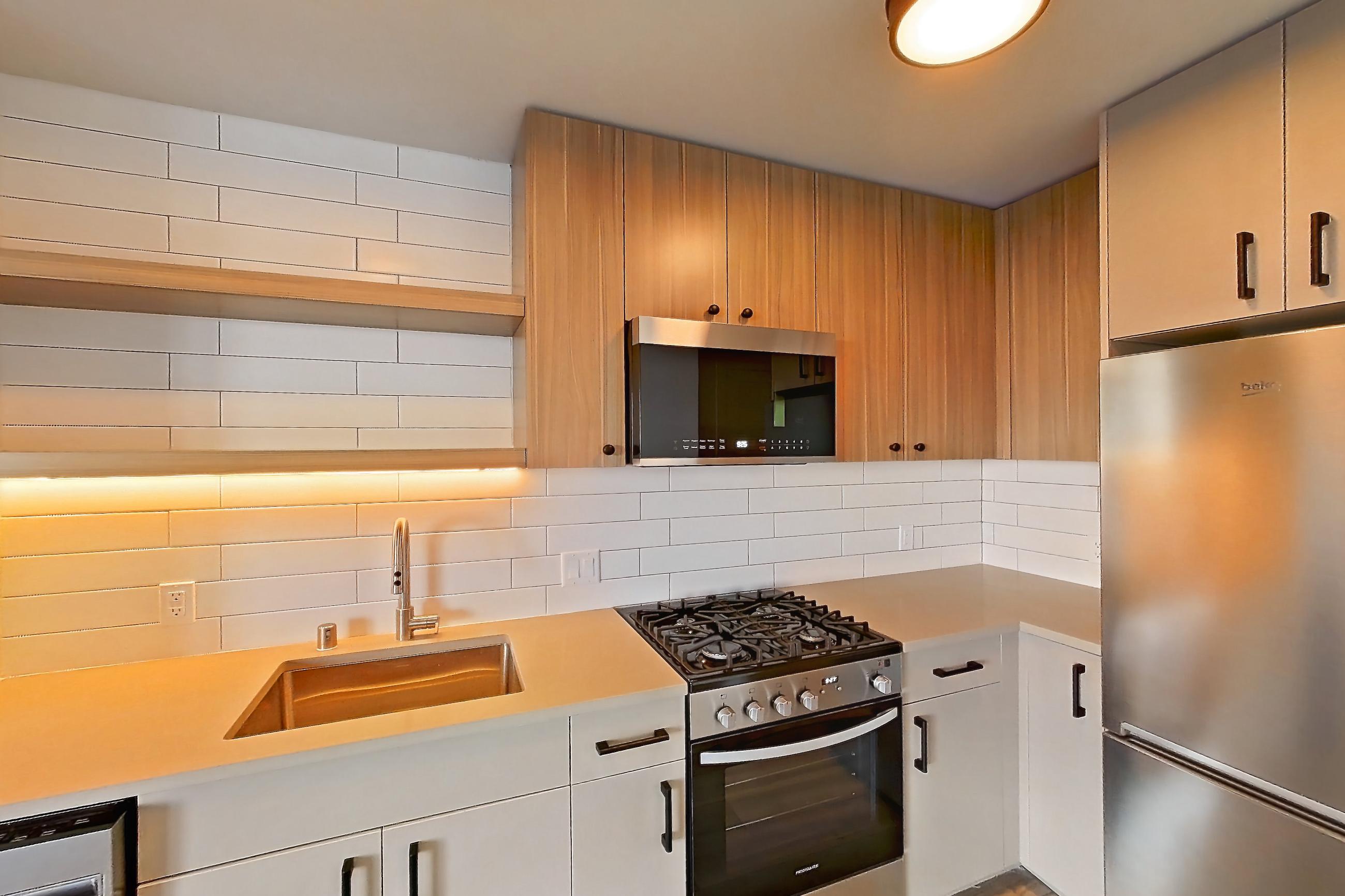Kitchen with dishwasher, gas range, light countertops, light wood-finish flooring, oven/range, refrigerator, and stainless steel appliances, Apartment 220 at The Myles
