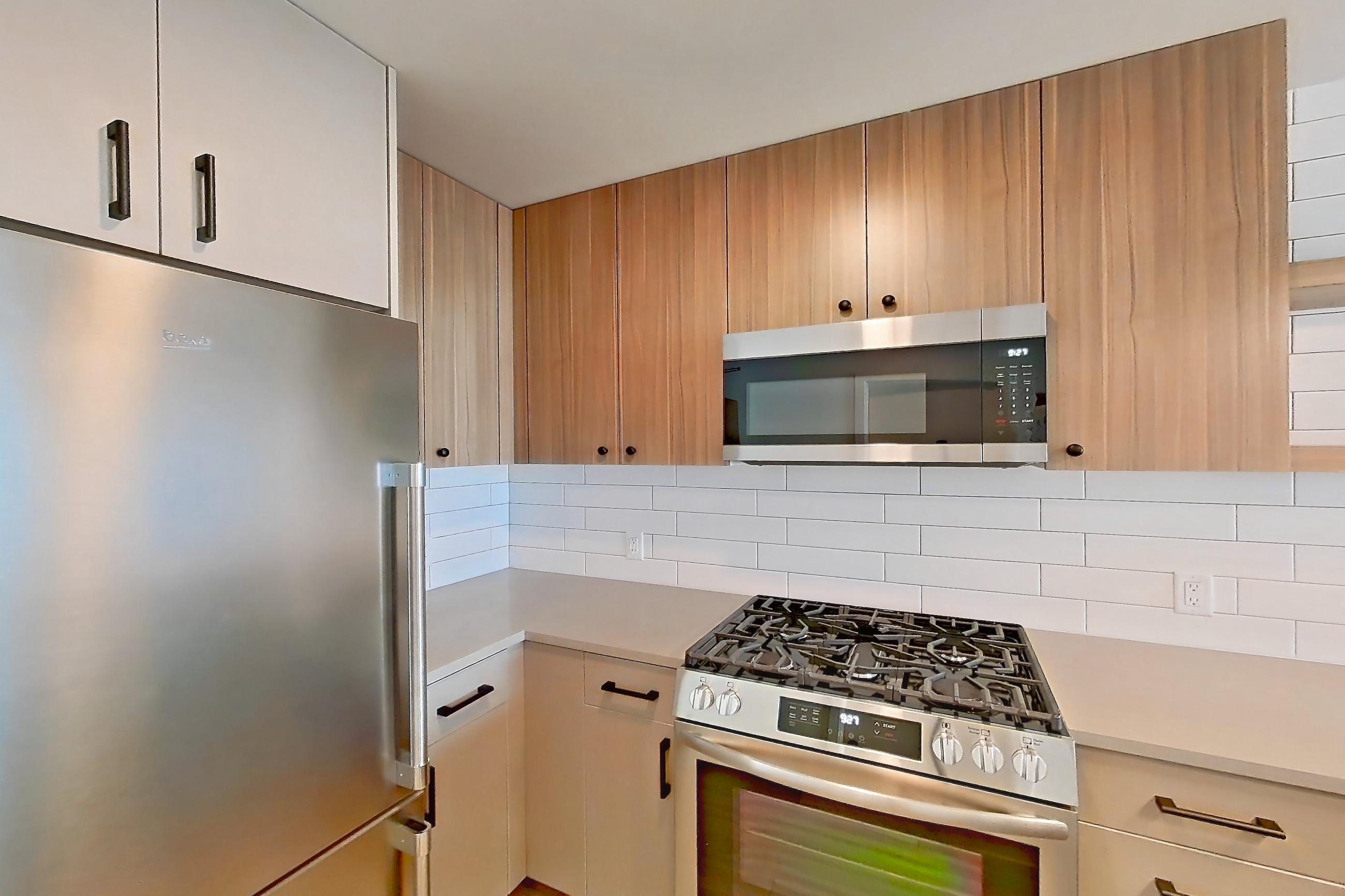 Kitchen with dishwasher, gas range, light countertops, light wood-finish flooring, oven/range, refrigerator, and stainless steel appliances, Apartment 223 at The Myles