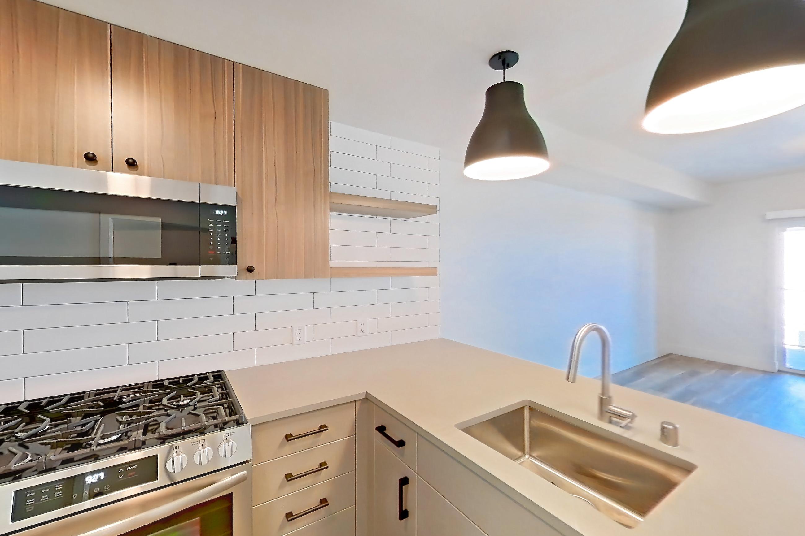 Kitchen with dishwasher, gas range, light countertops, light wood-finish flooring, oven/range, refrigerator, and stainless steel appliances, Apartment 223 at The Myles