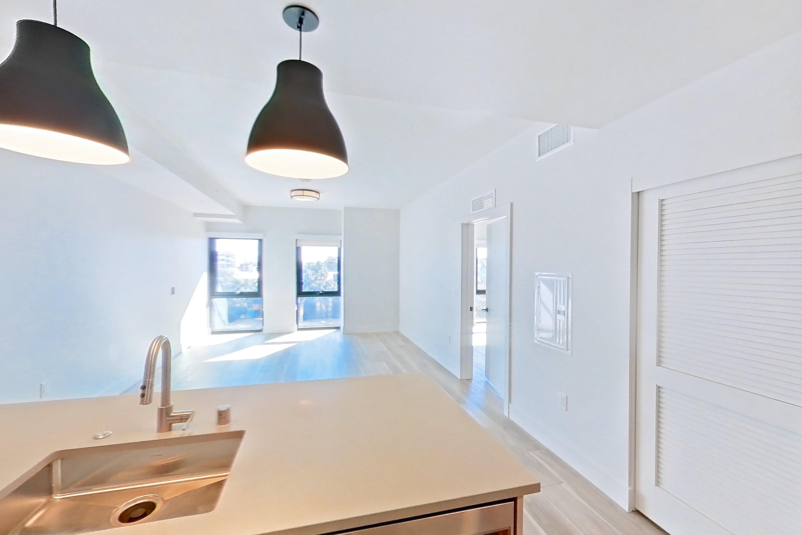 Kitchen with dishwasher, gas range, light countertops, light wood-finish flooring, oven/range, range hood, refrigerator, and stainless steel appliances, Apartment 225 at The Myles