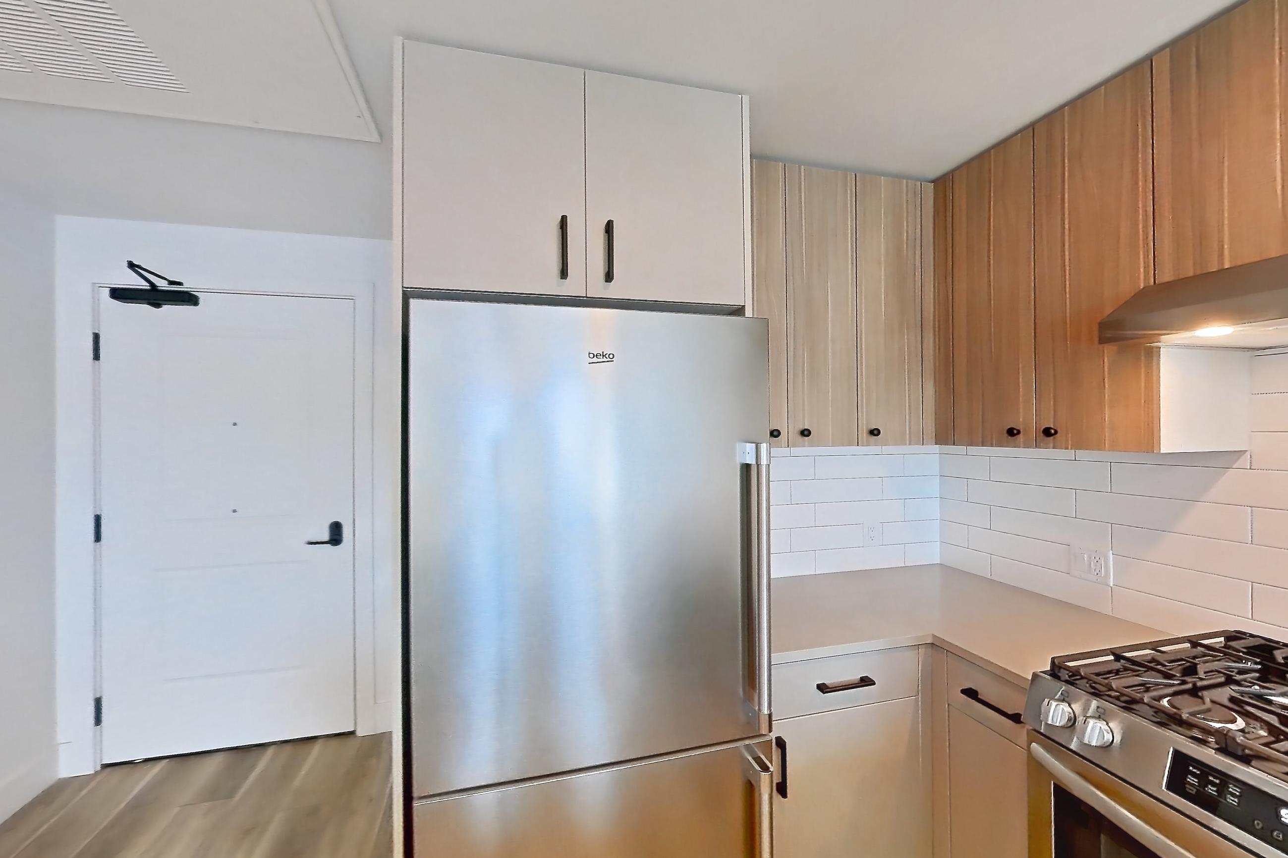 Kitchen with dishwasher, gas range, light countertops, light wood-finish flooring, oven/range, range hood, refrigerator, and stainless steel appliances, Apartment 225 at The Myles