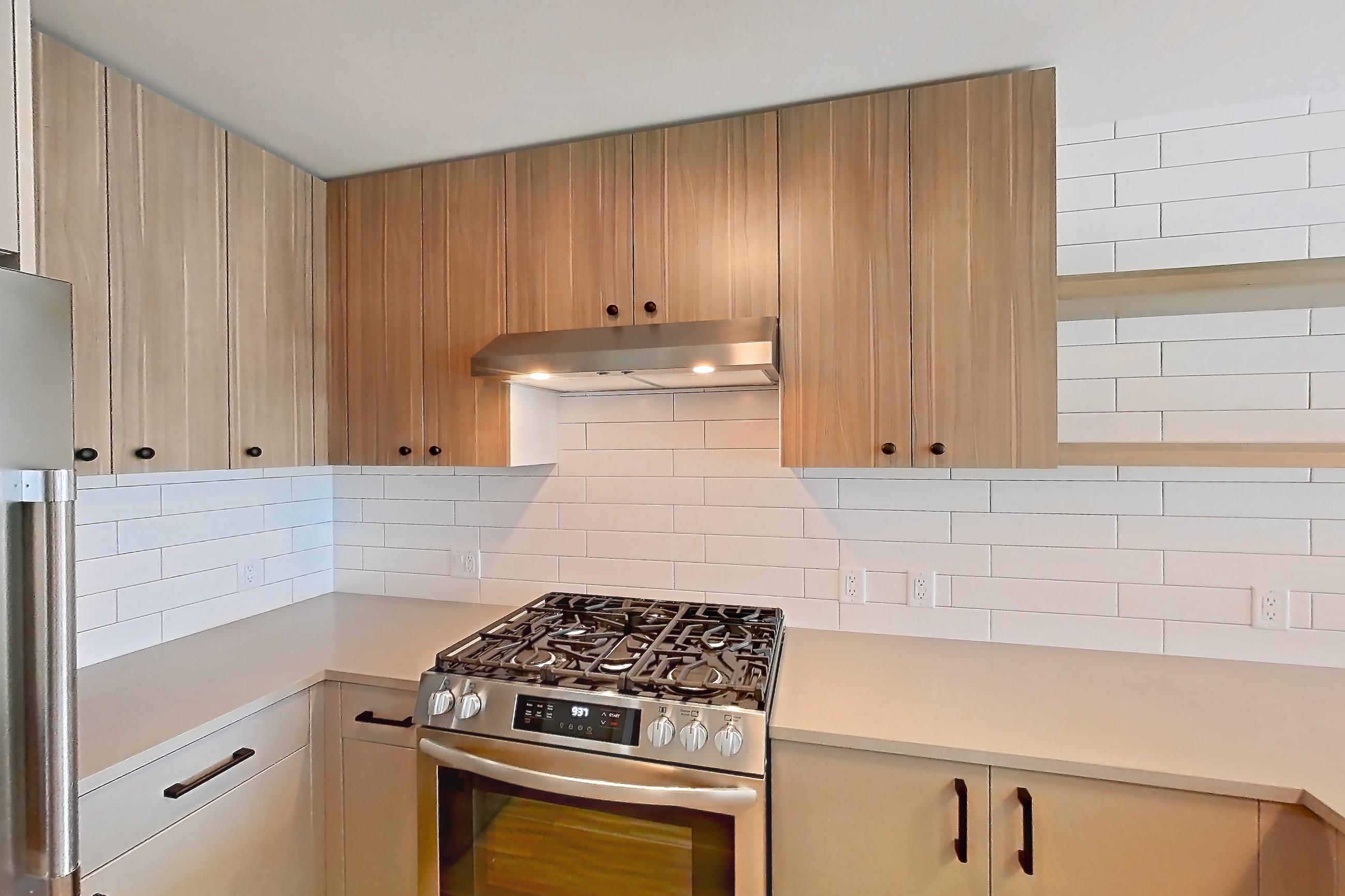 Kitchen with dishwasher, gas range, light countertops, light wood-finish flooring, oven/range, range hood, refrigerator, and stainless steel appliances, Apartment 225 at The Myles