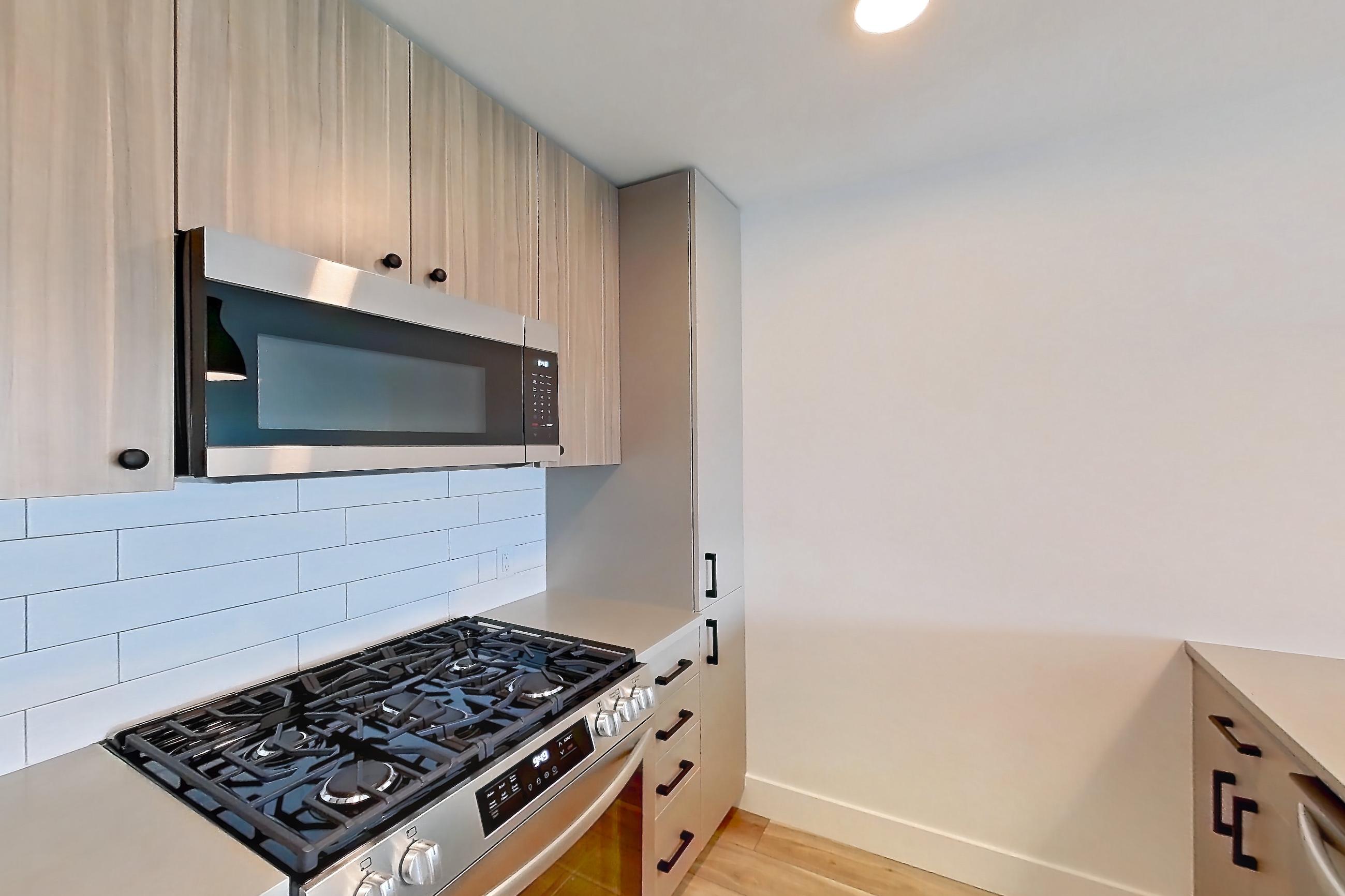 Kitchen with dishwasher, gas range, light countertops, light wood-finish flooring, microwave, oven/range, refrigerator, and stainless steel appliances, Apartment 230 at The Myles
