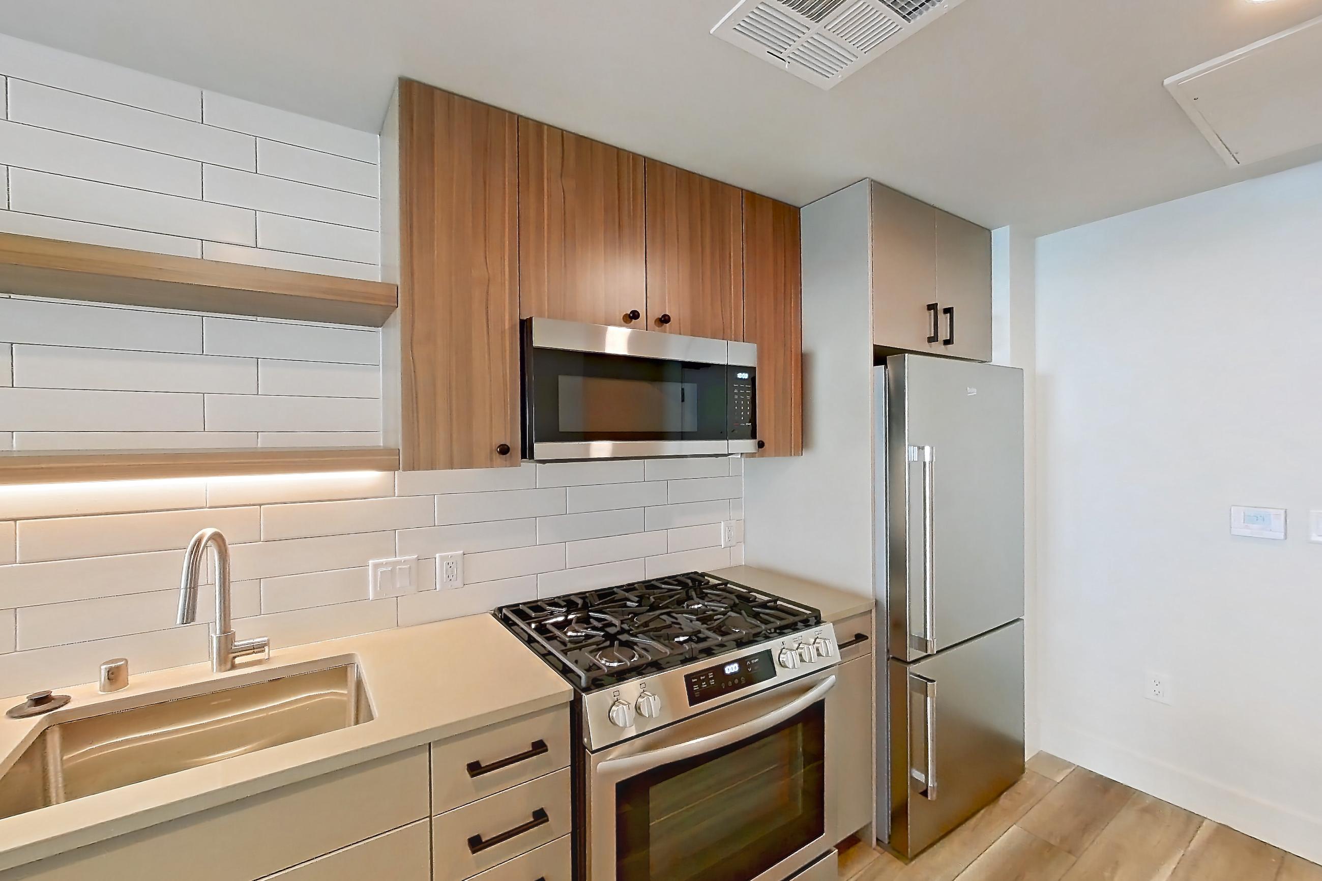 Kitchen with dishwasher, gas range, light countertops, light wood-finish flooring, microwave, oven/range, refrigerator, and stainless steel appliances, Apartment 234 at The Myles