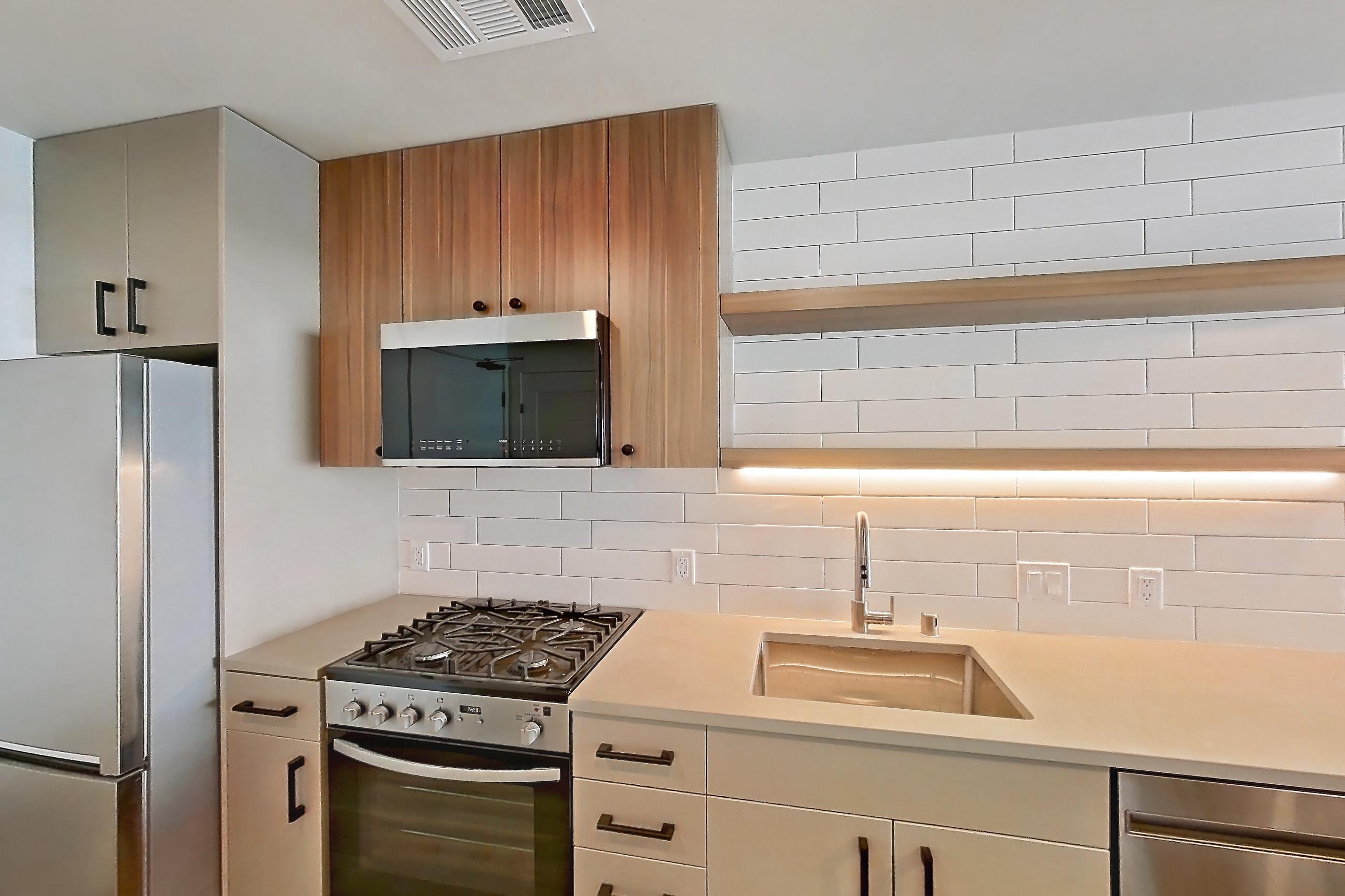 Kitchen with dishwasher, gas range, light countertops, light stone countertops, light wood-finish flooring, oven/range, refrigerator, and stainless steel appliances, Apartment 235 at The Myles