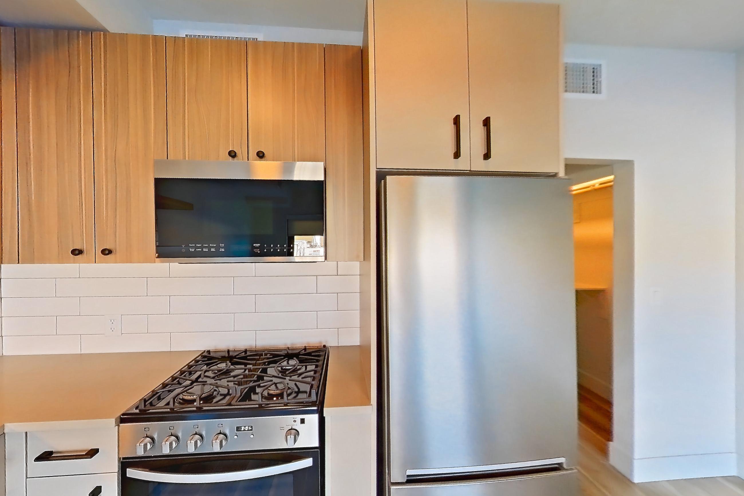 Kitchen with dishwasher, gas range, light countertops, light wood-finish flooring, oven/range, refrigerator, and stainless steel appliances, Apartment 253 at The Myles